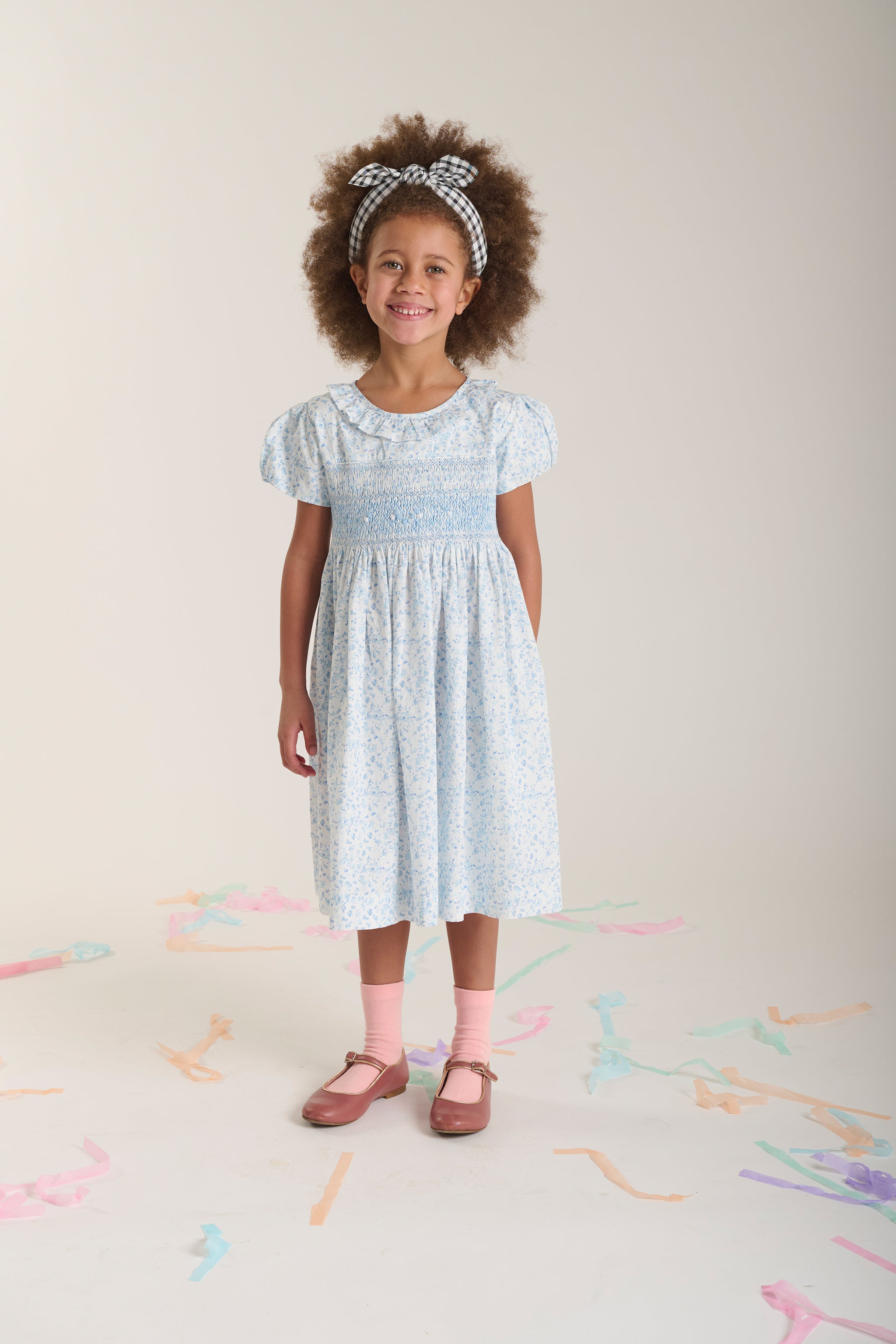 Young girl wearing a white hand-smocked dress with delicate blue floral pattern