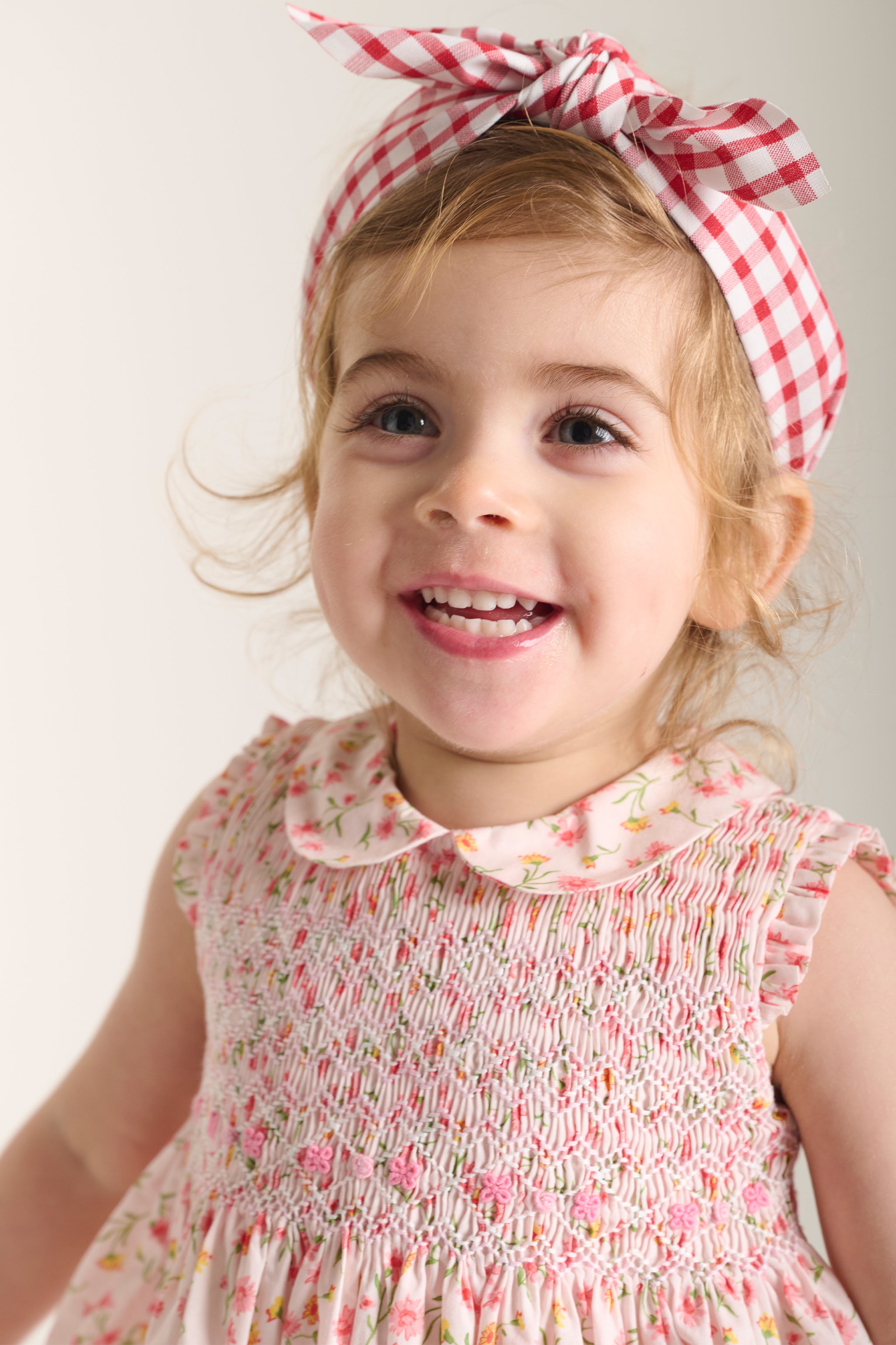 Young girl wearing a floral dress and checkered headband with a plain background