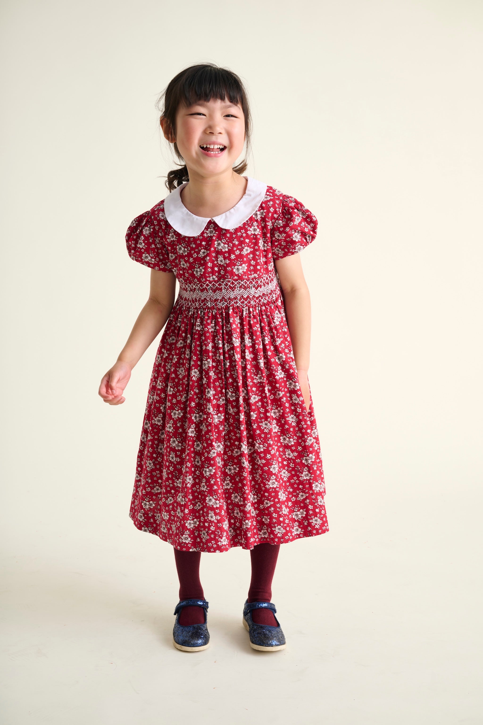 Young girl wearing a red floral dress with a white collar on a beige background