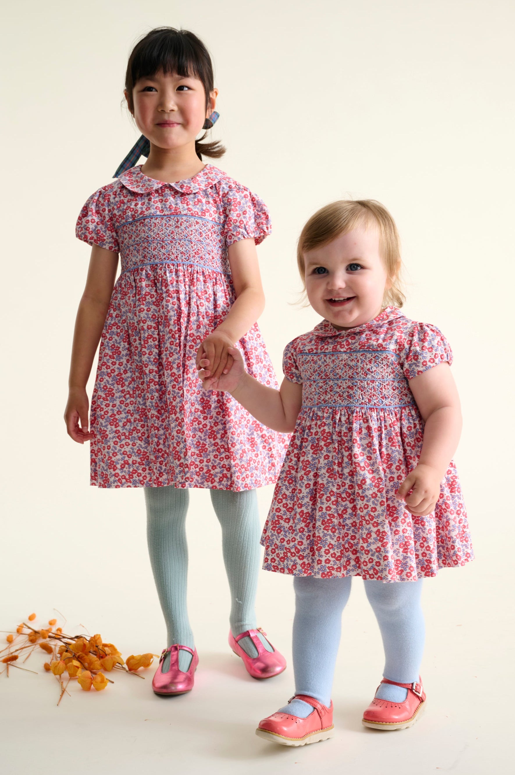 Two children wearing matching red and blue floral dresses holding hands