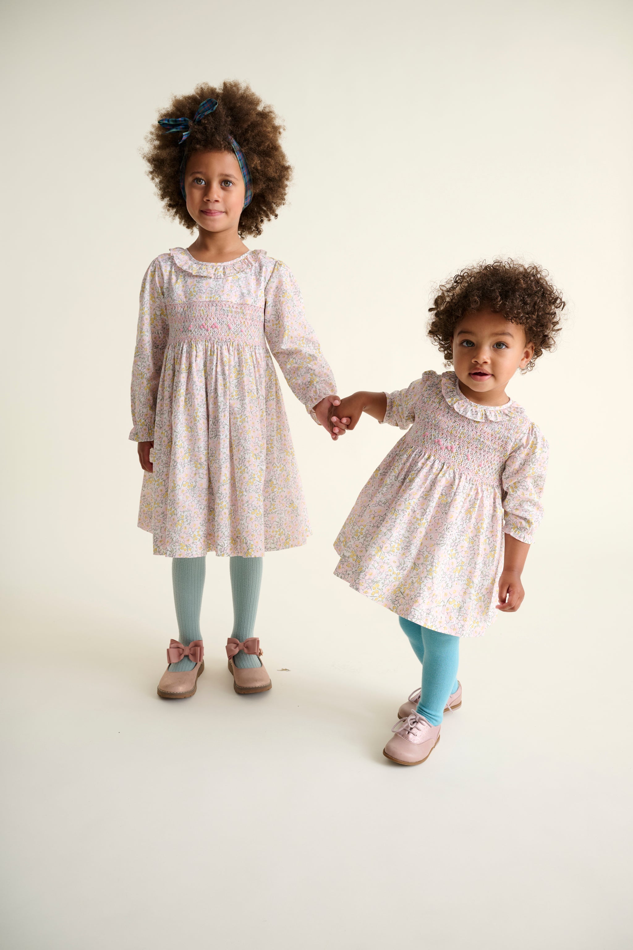 Two young girls in matching dresses standing against a plain background
