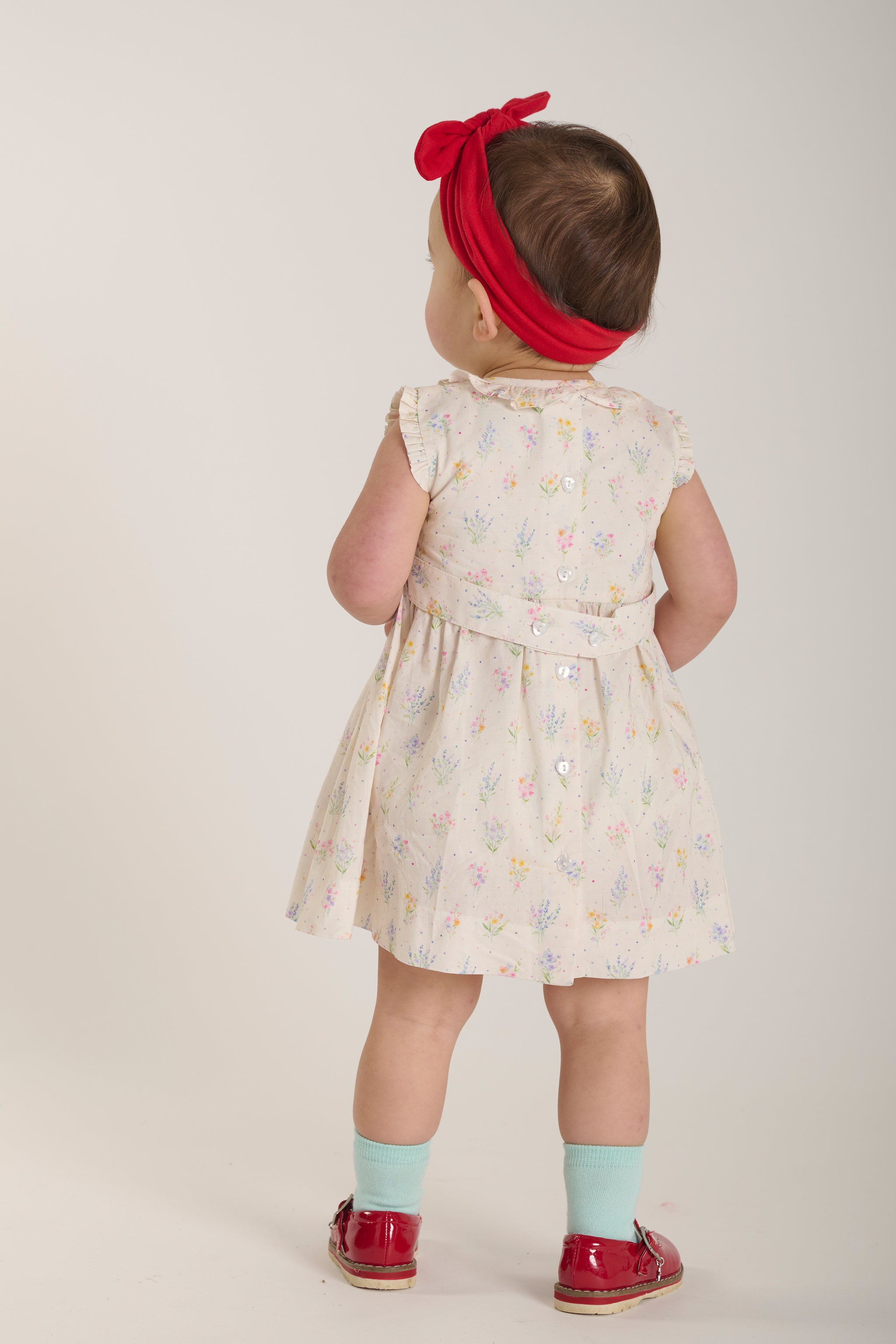 Child wearing a floral dress with a red headband on a plain background