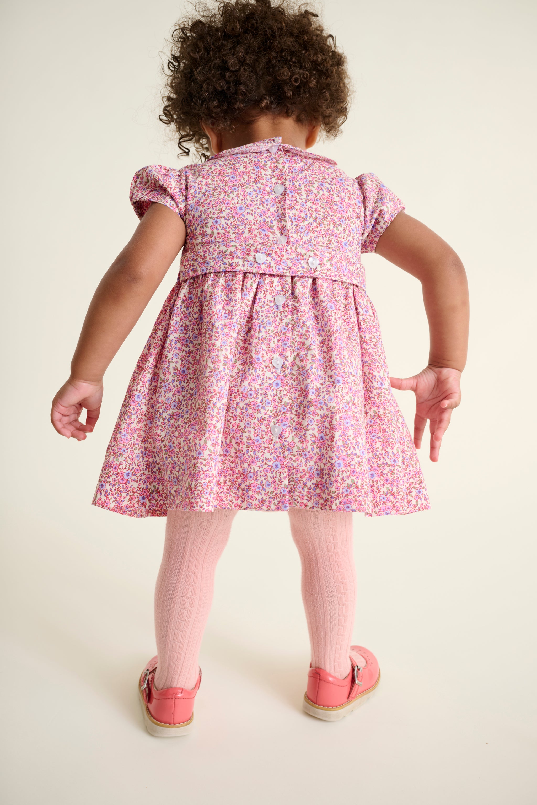 Child wearing a pink floral dress showcasing the back of dress with heart shaped buttons