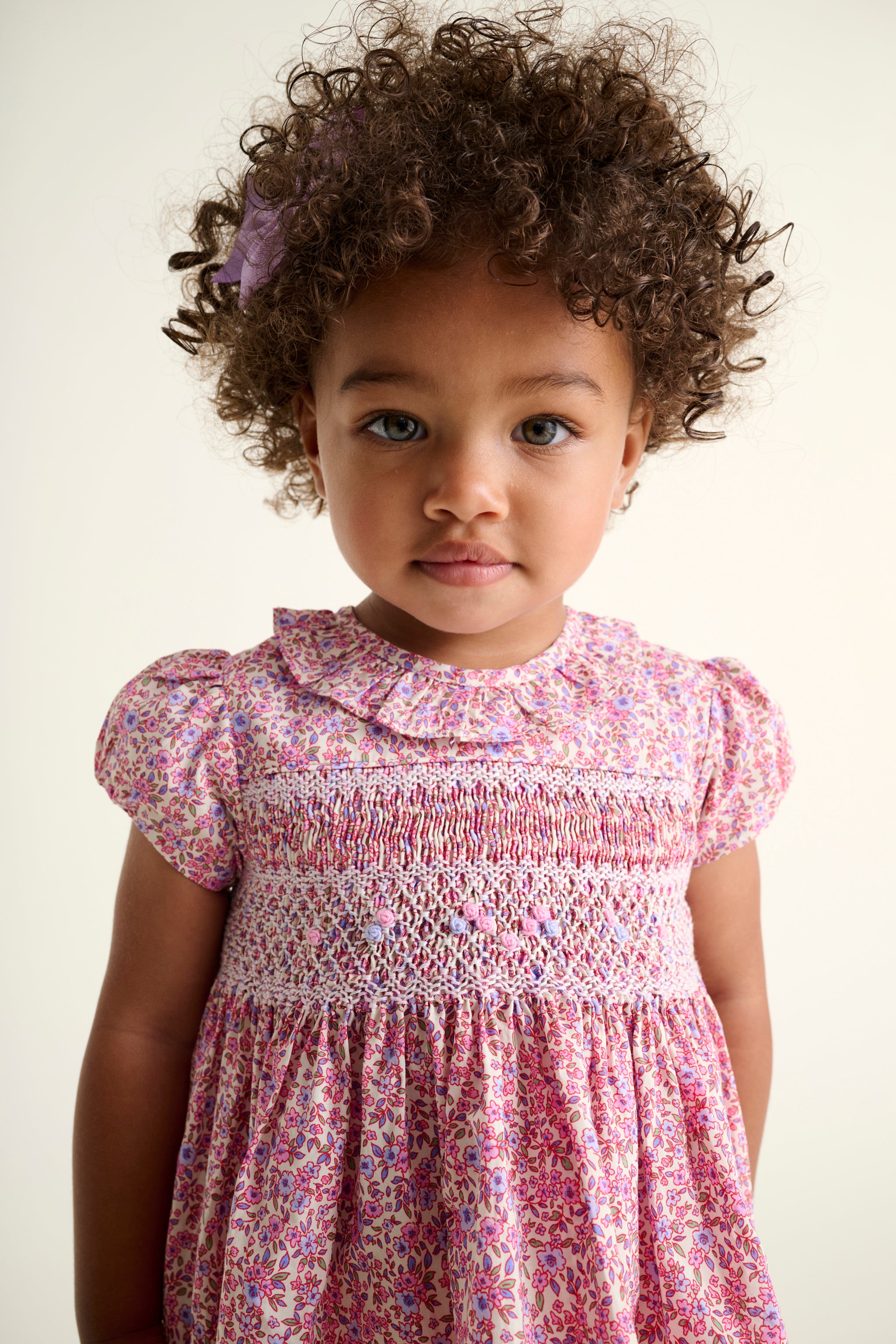 toddler girl in a pink ditzy floral hand-smocked dress
