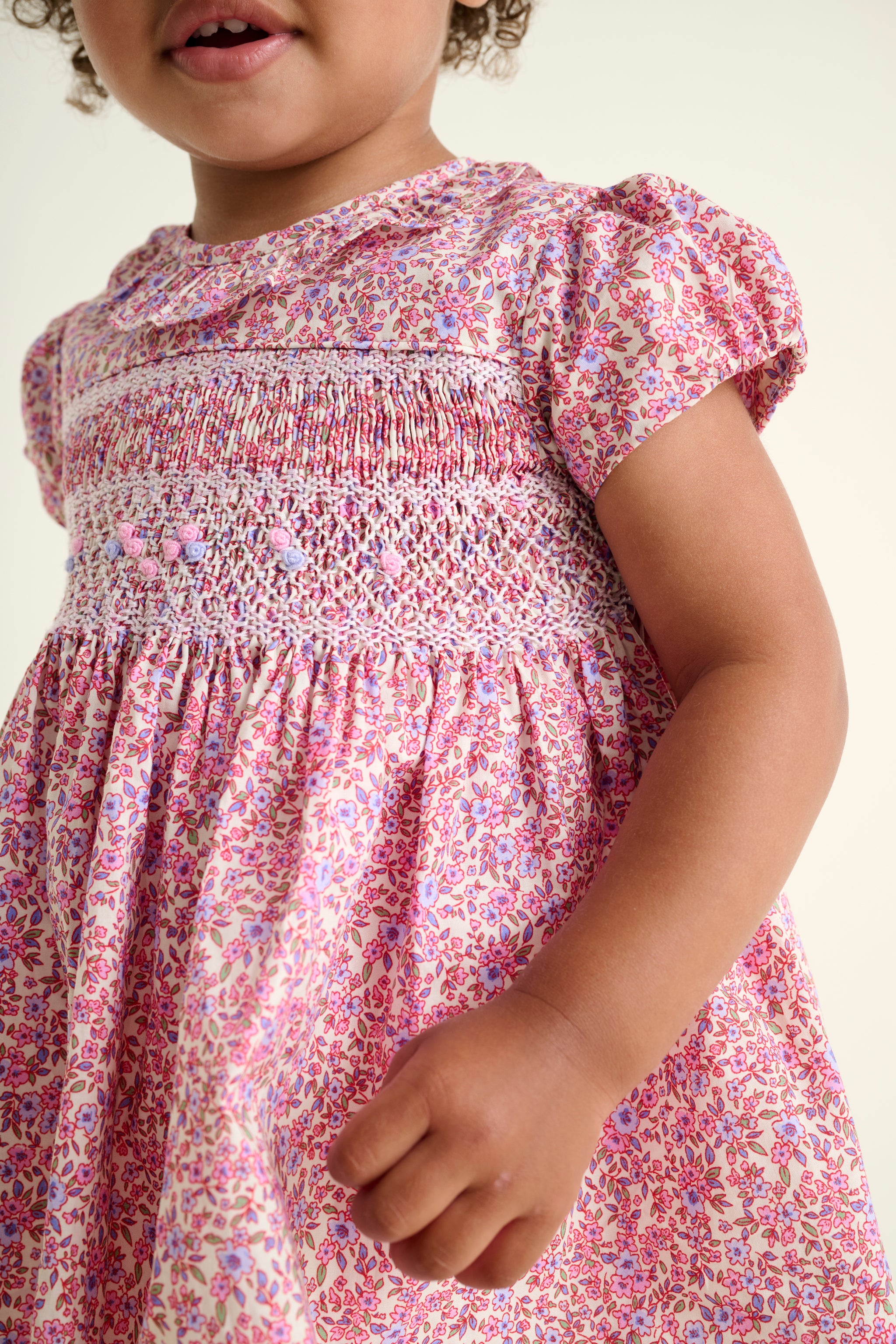 Close-up of a child wearing a pink floral dress with smocked details.