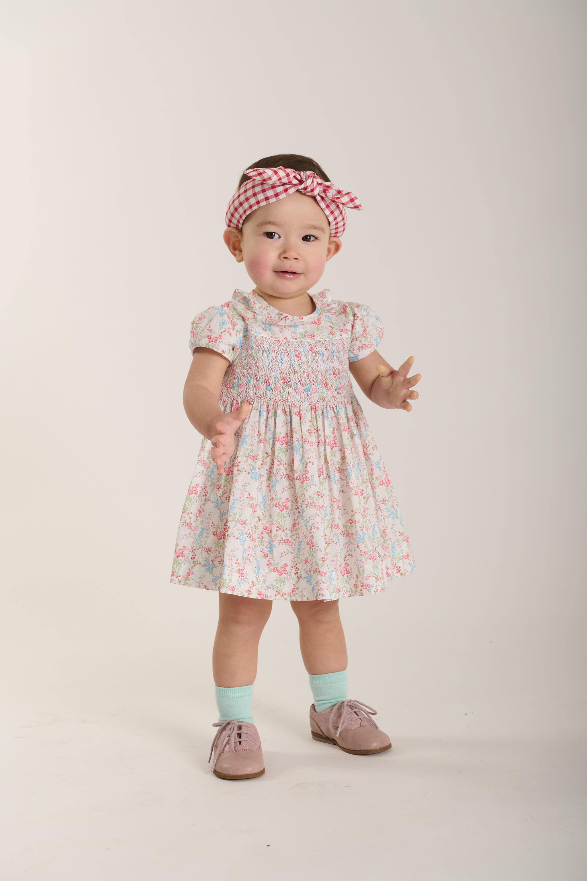 Baby wearing a floral dress and headband on a plain background