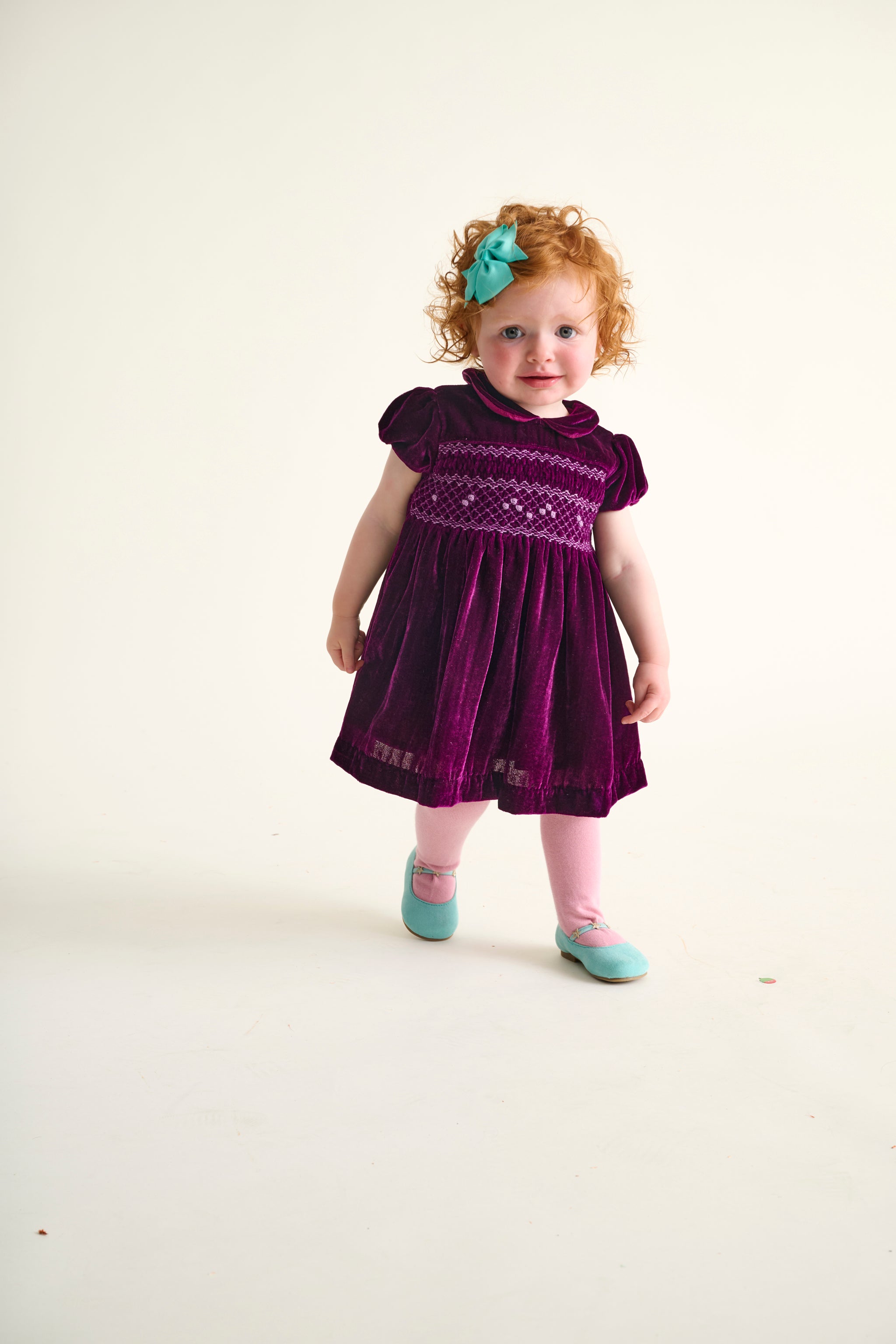 Toddler girl wearing a burgundy velvet party dress with hand-smocking