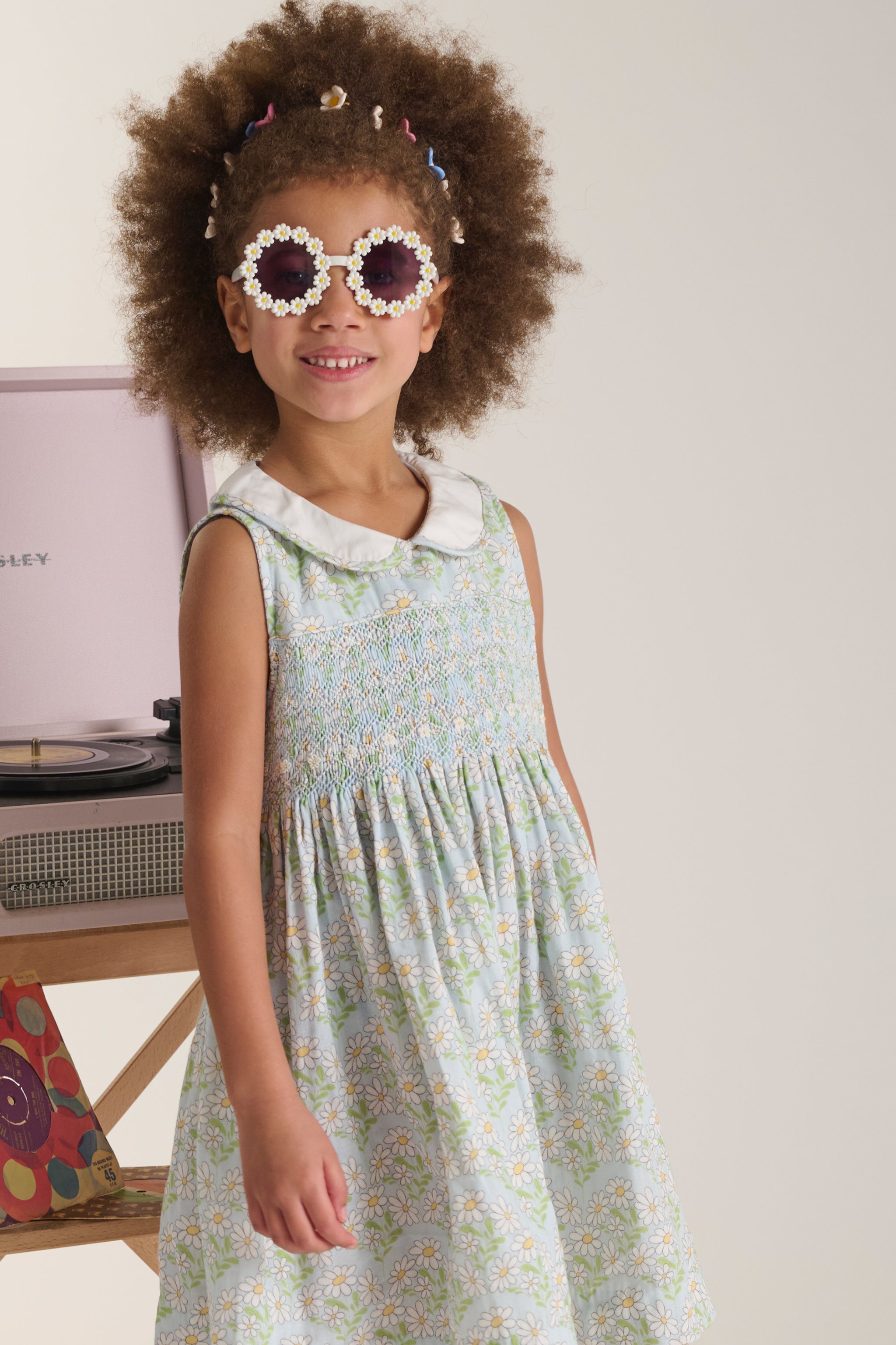 Young girl wearing a blue daisy smock dress and daisy sunglasses