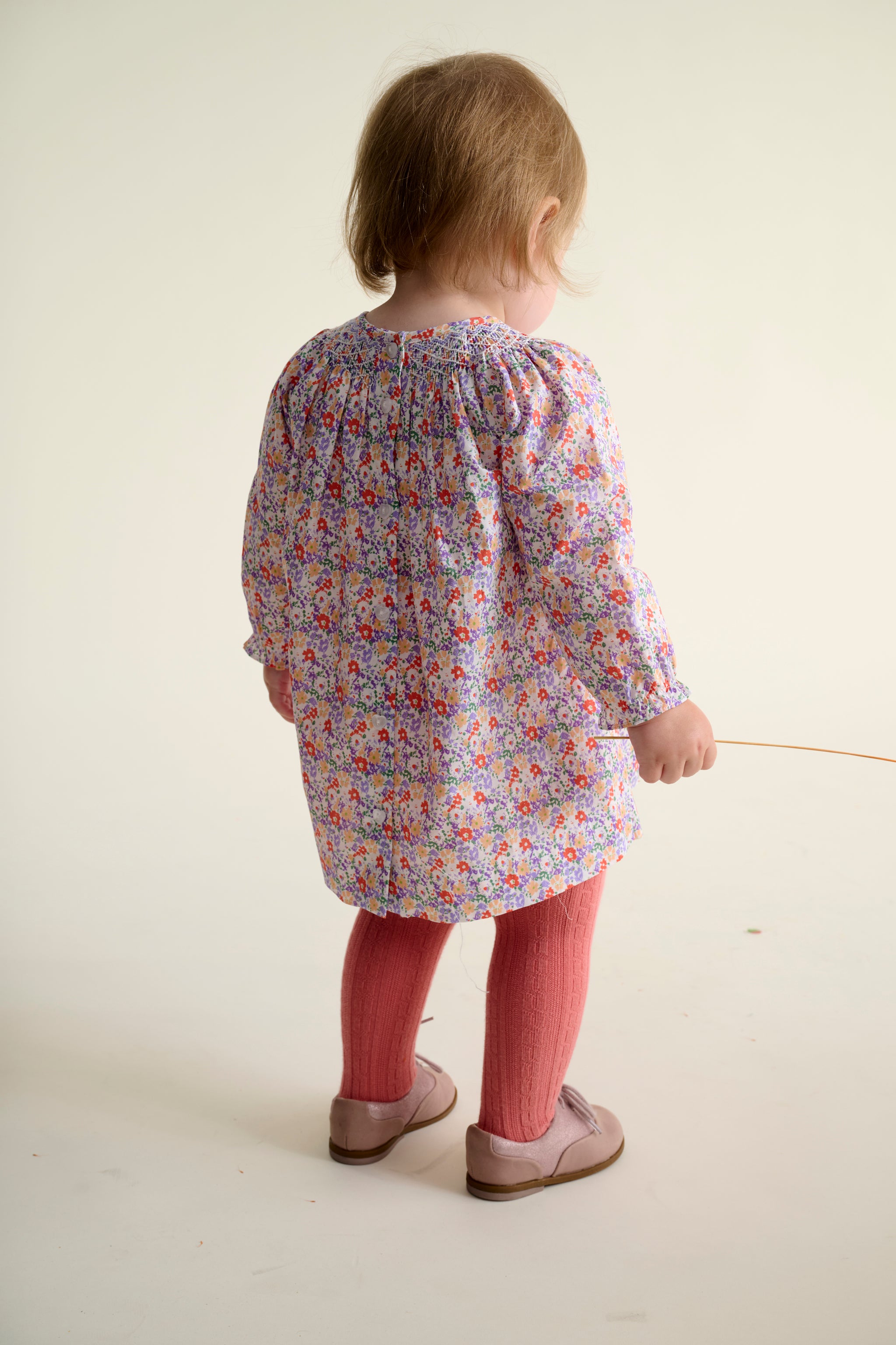 Toddler girl wearing a floral dress with long sleeves and hand-smocking