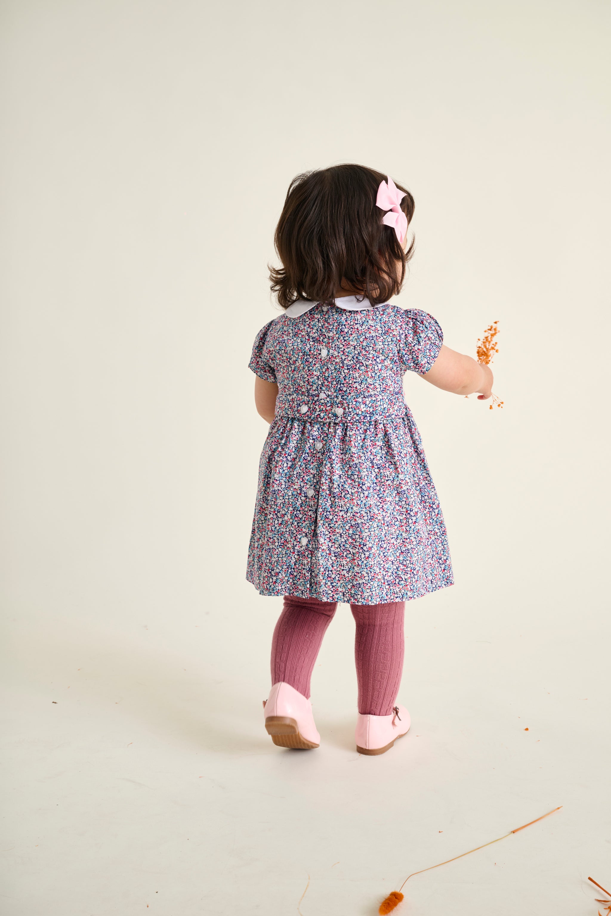 Child wearing a floral dress and pink tights on a plain background