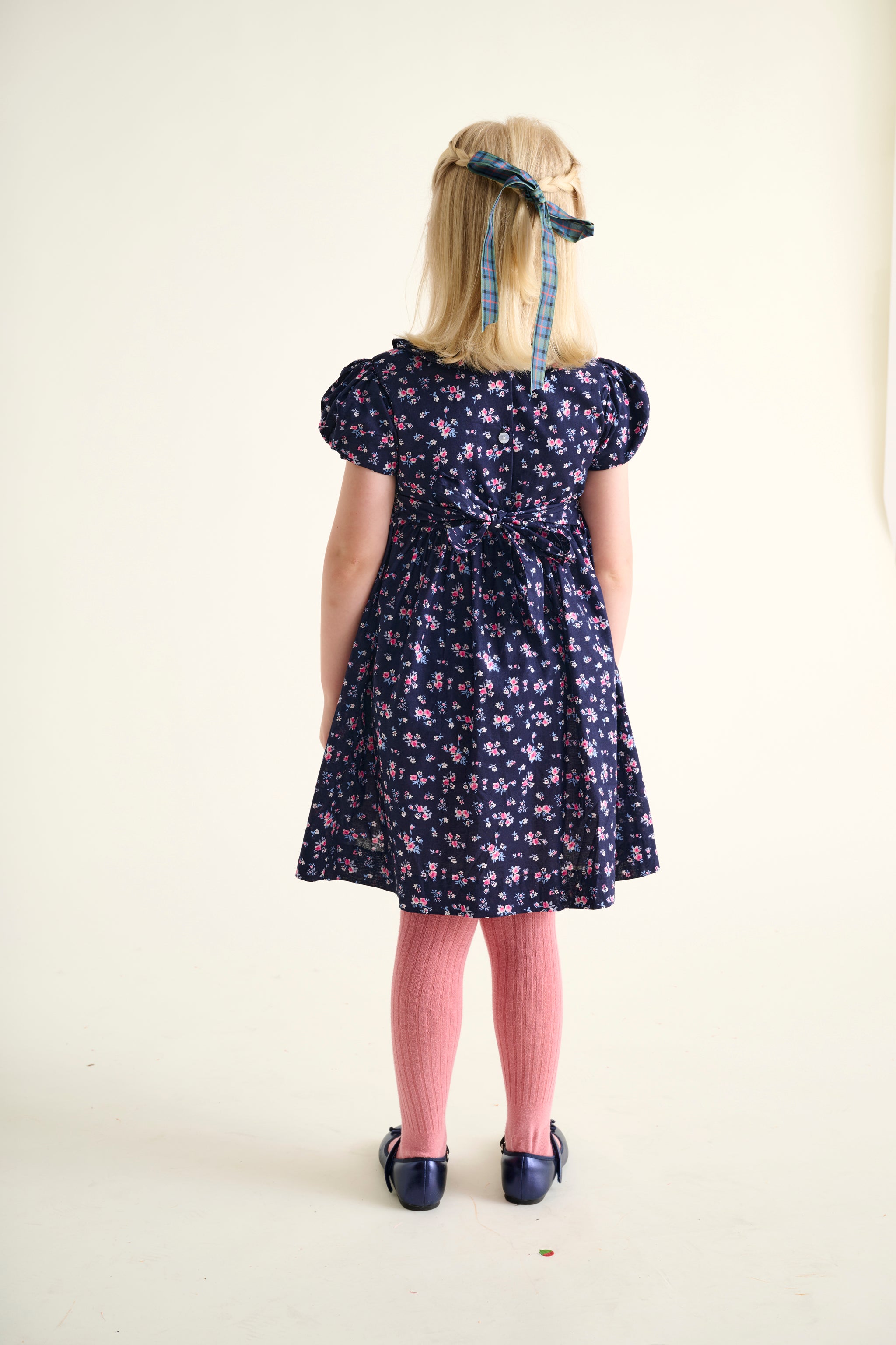 Young girl wearing a floral dress with puffed sleeves and pink tights on a white background