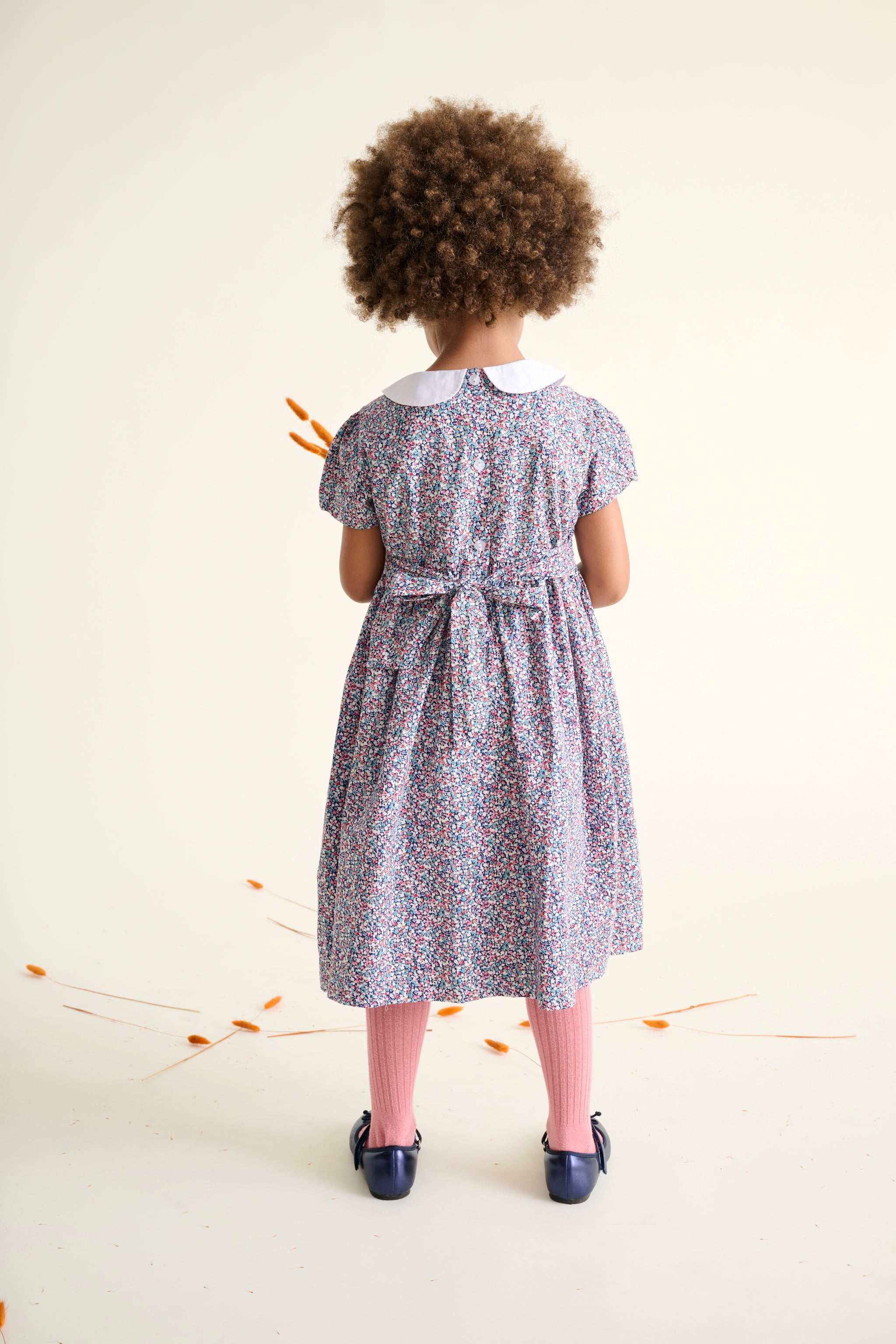 back view of child wearing a floral dress with a white collar against a plain background