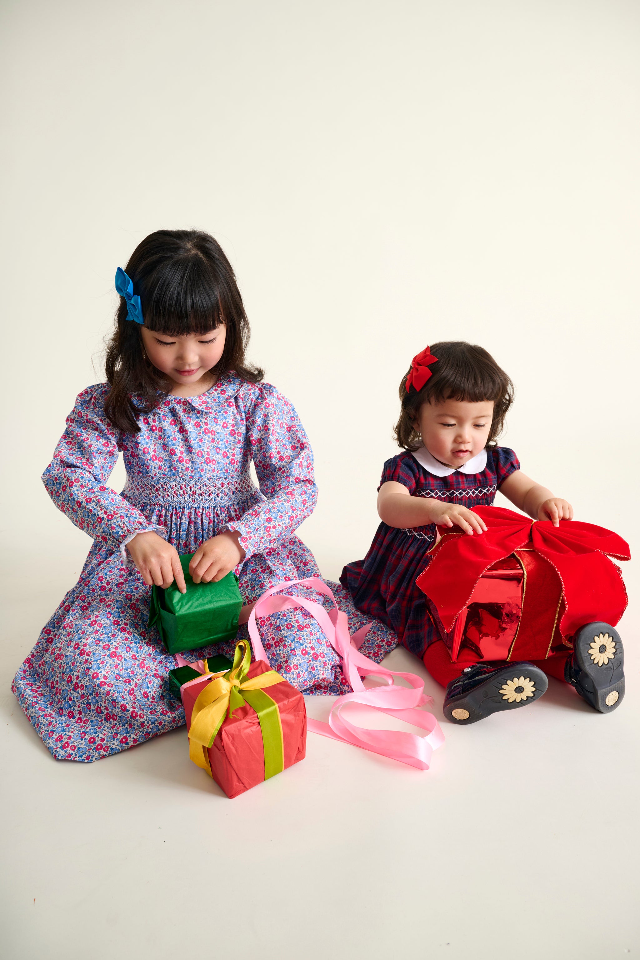 Two young girls playing with toys on a white background wearing festive dresses