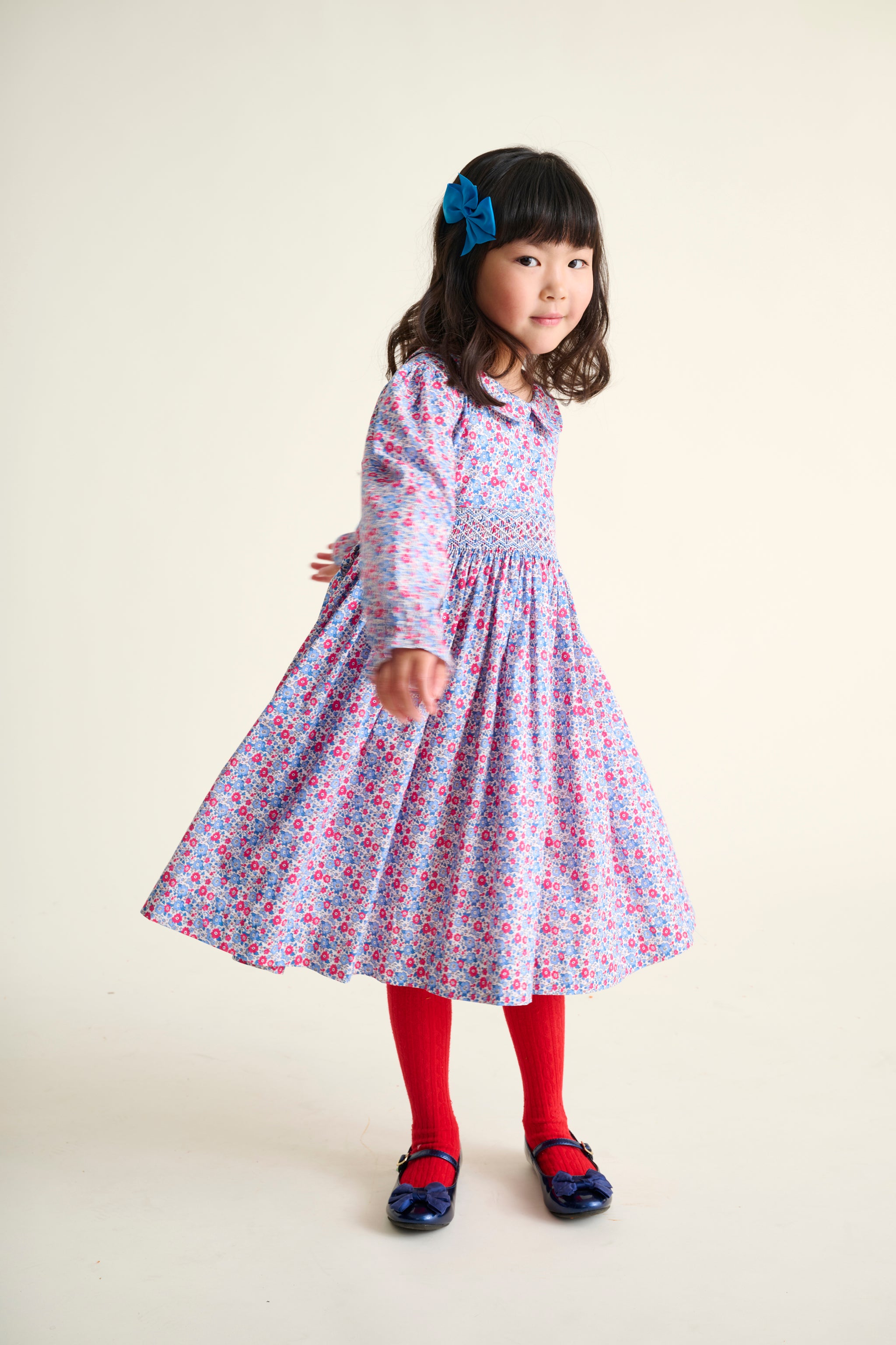 Young girl wearing a floral dress with red tights and blue shoes on a white background