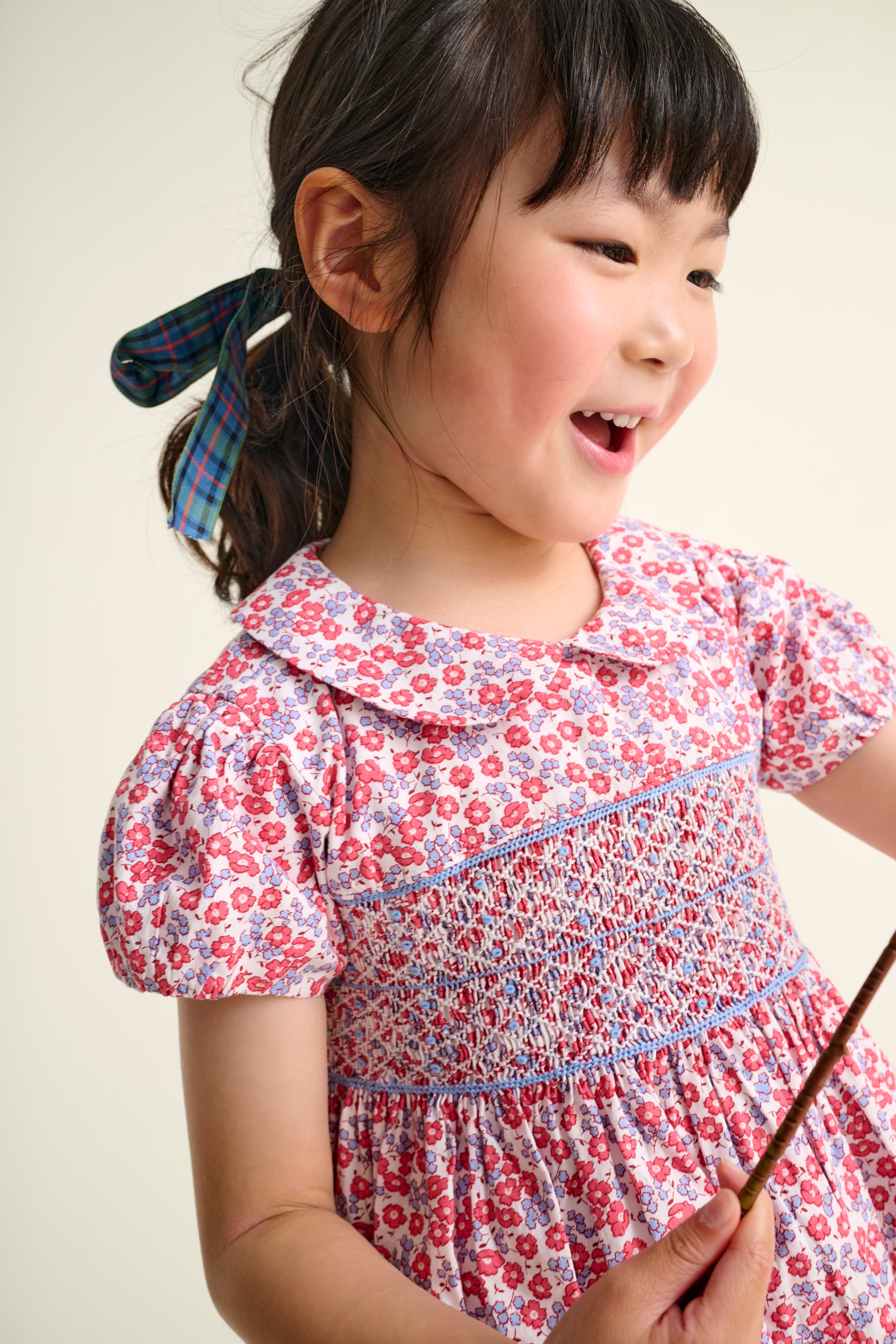 girl in a floral dress holding a twig against a plain background