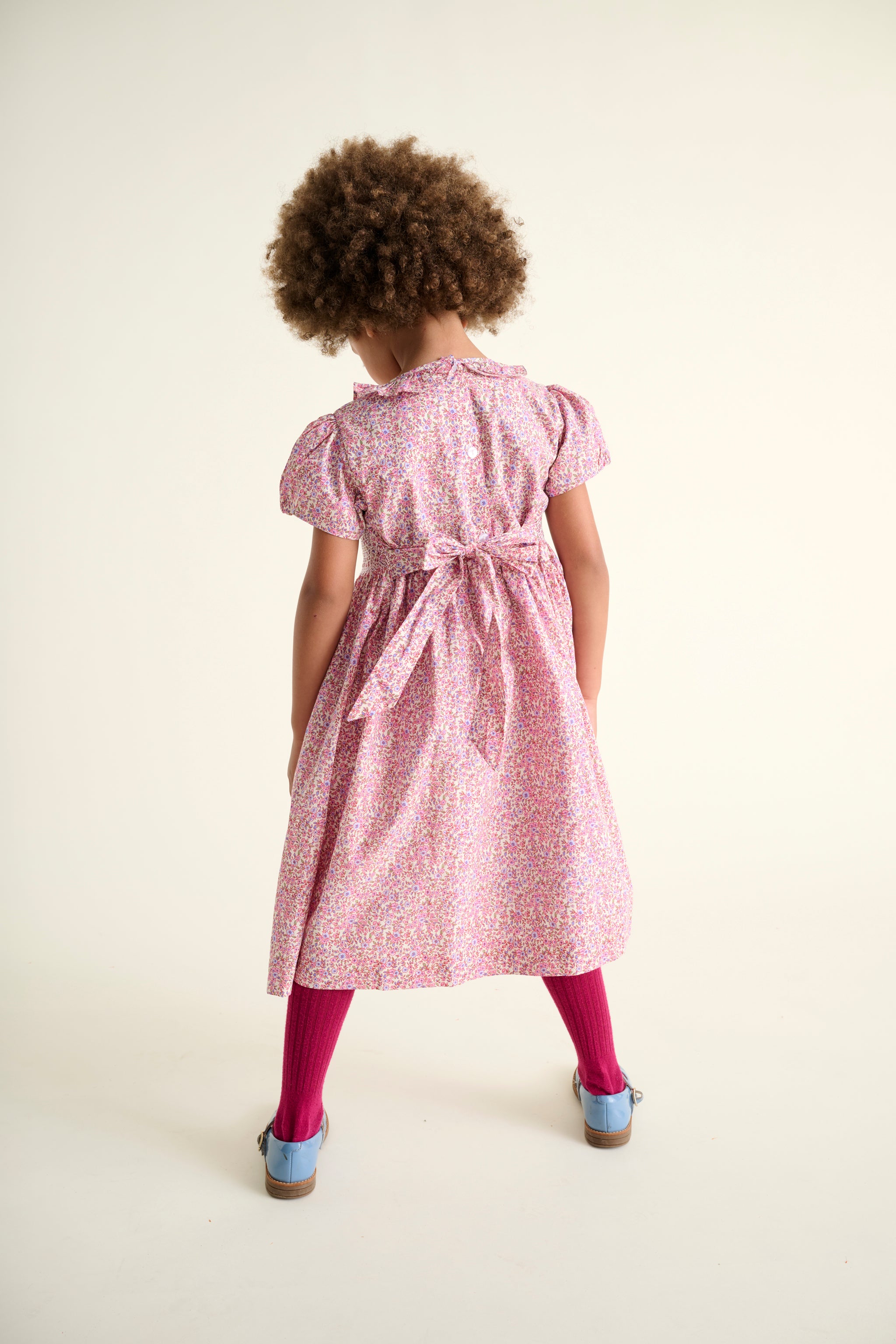 Child wearing a pink floral dress standing with back to viewer