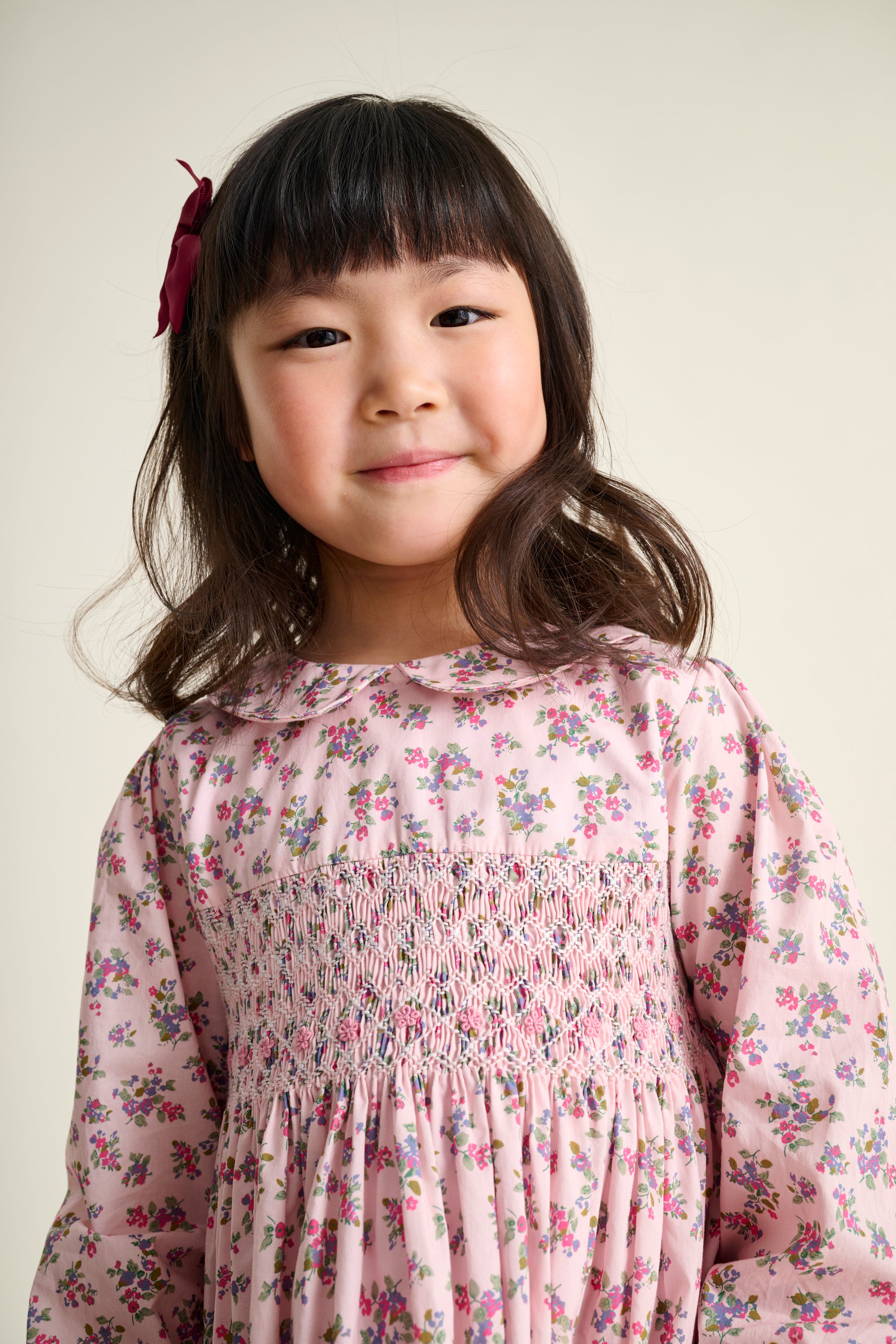 Young girl wearing a floral hand-smocked dress with a plain background