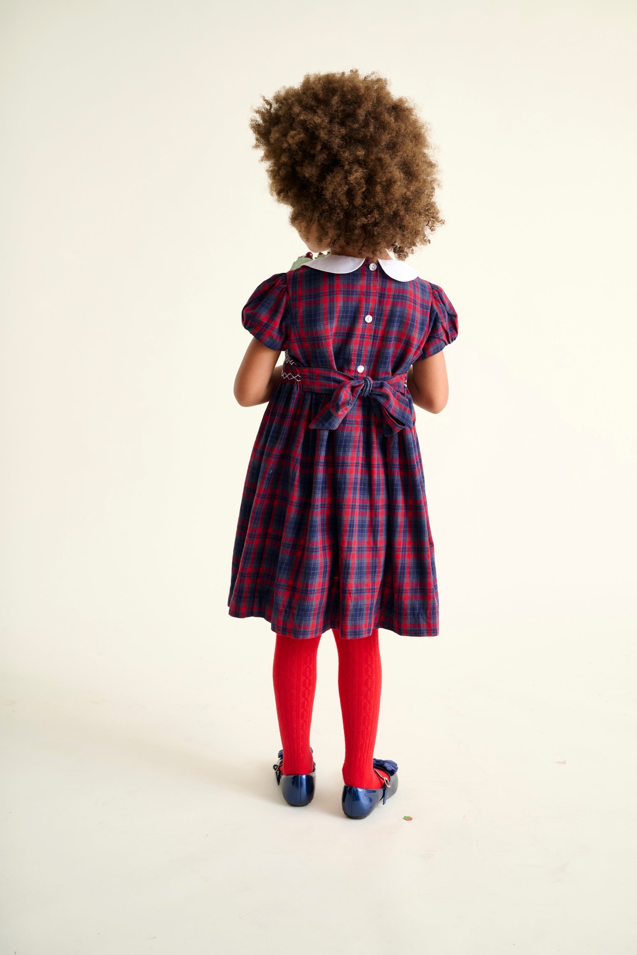 Child wearing a red and blue plaid dress with red tights on a white background