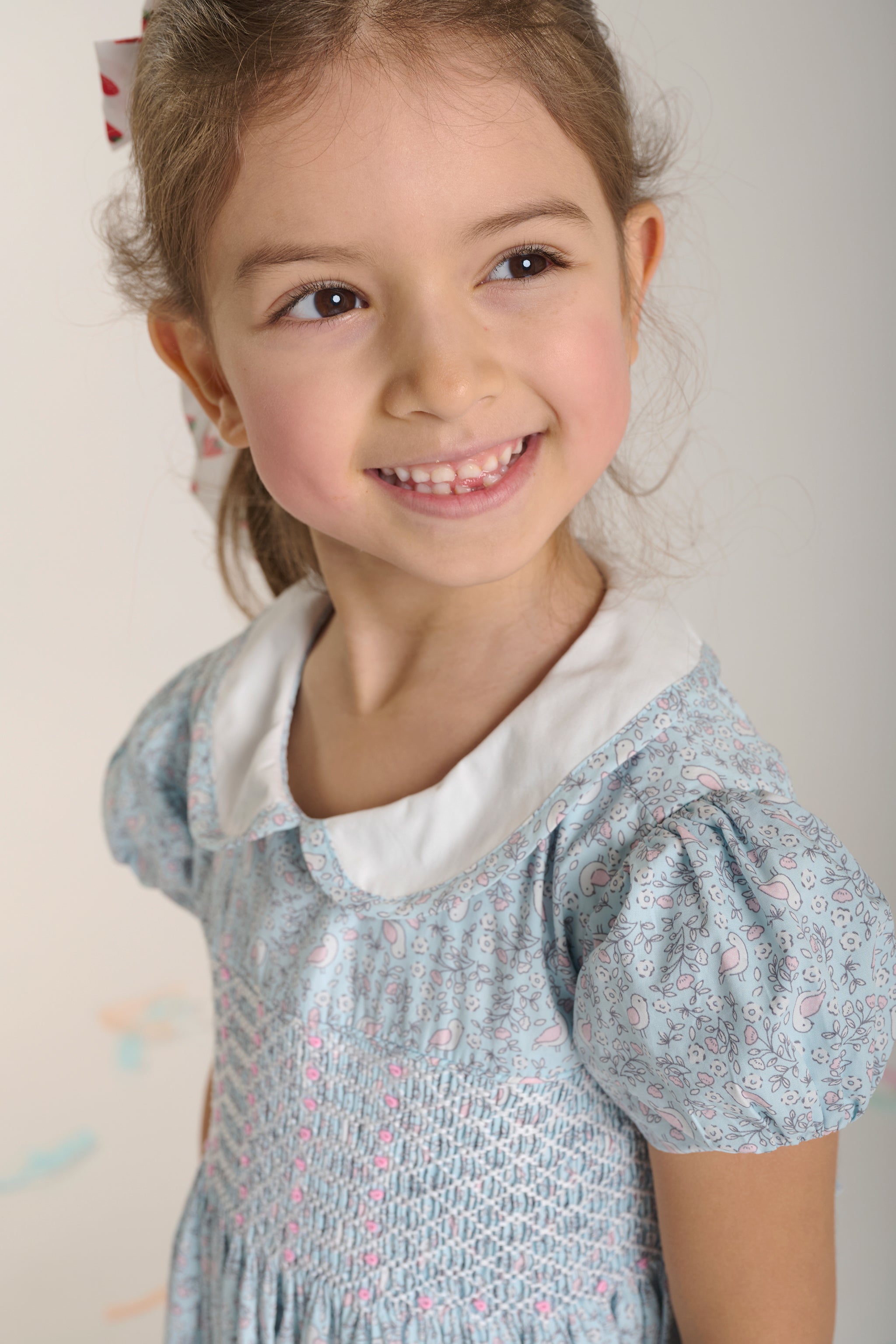Young girl wearing a light blue dress with white collar against a plain background