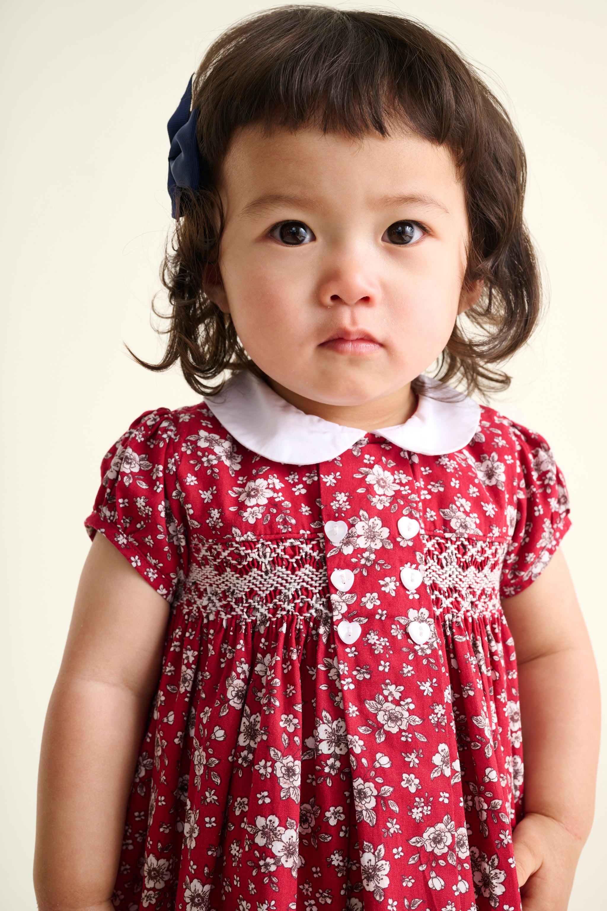 Child wearing a red floral dress with a white collar against a plain background