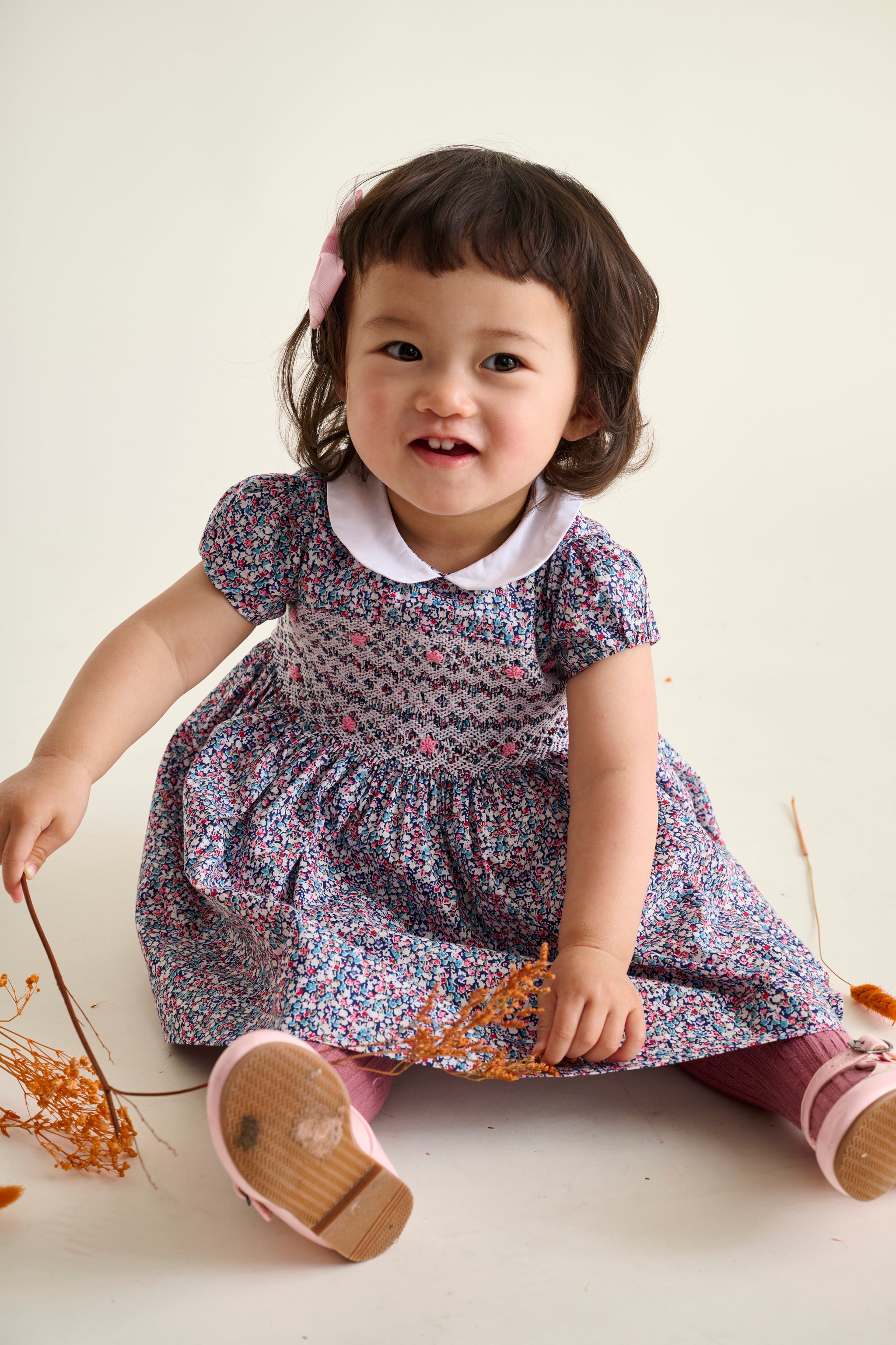 Child wearing a floral dress sitting and smiling