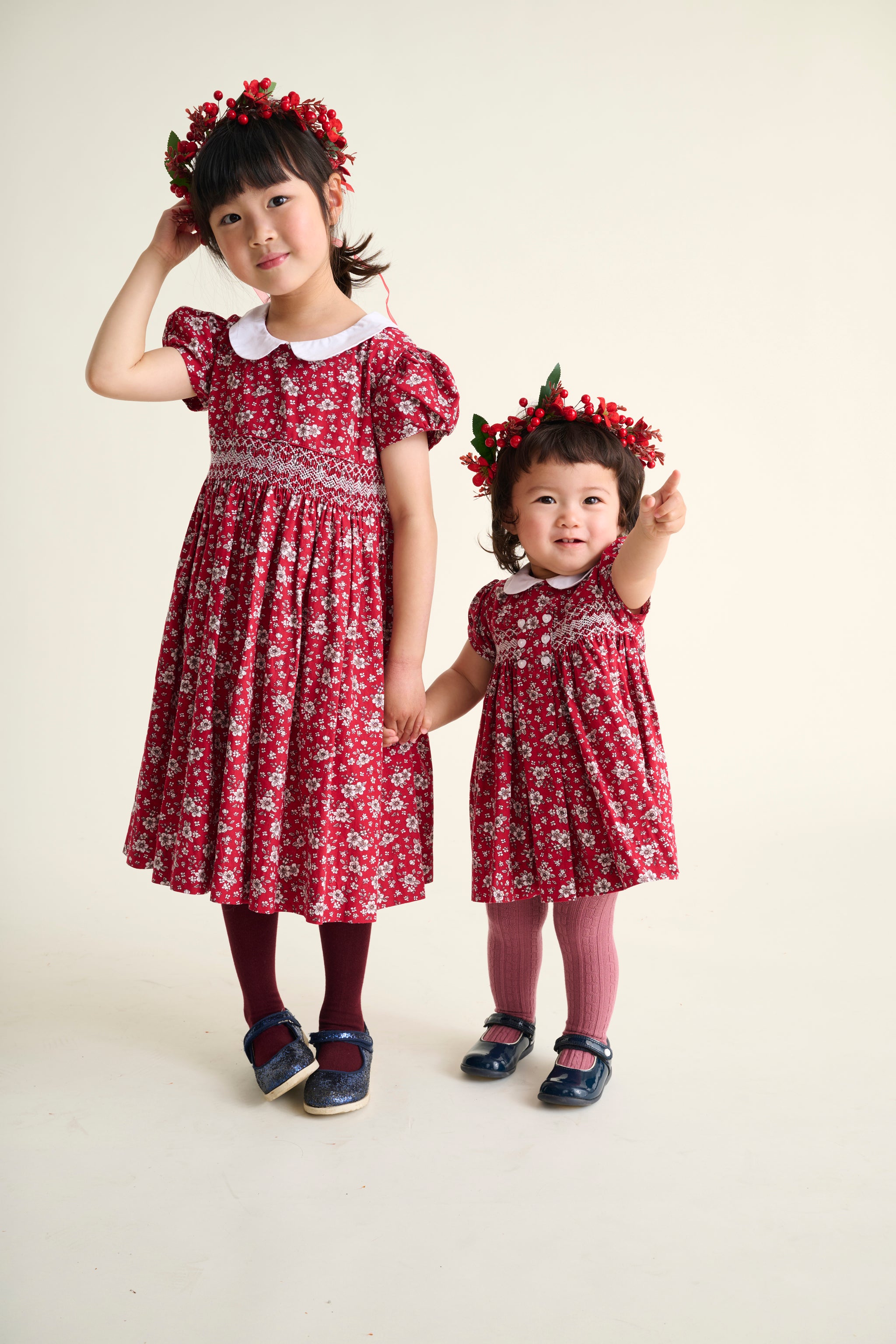 Two sisters wearing matching red floral dresses with hand smocking