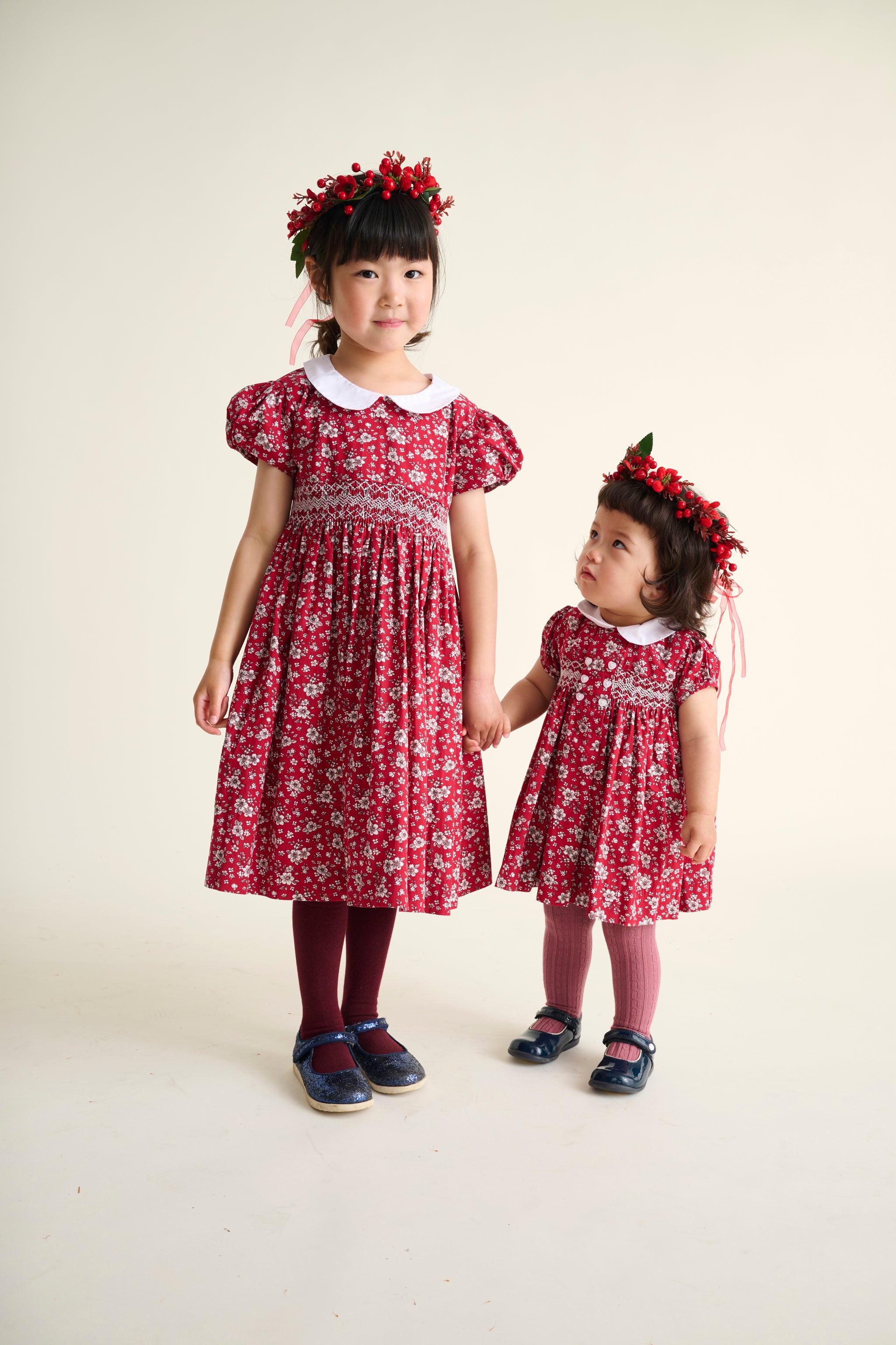 Two children wearing matching red floral smock dresses on a white background