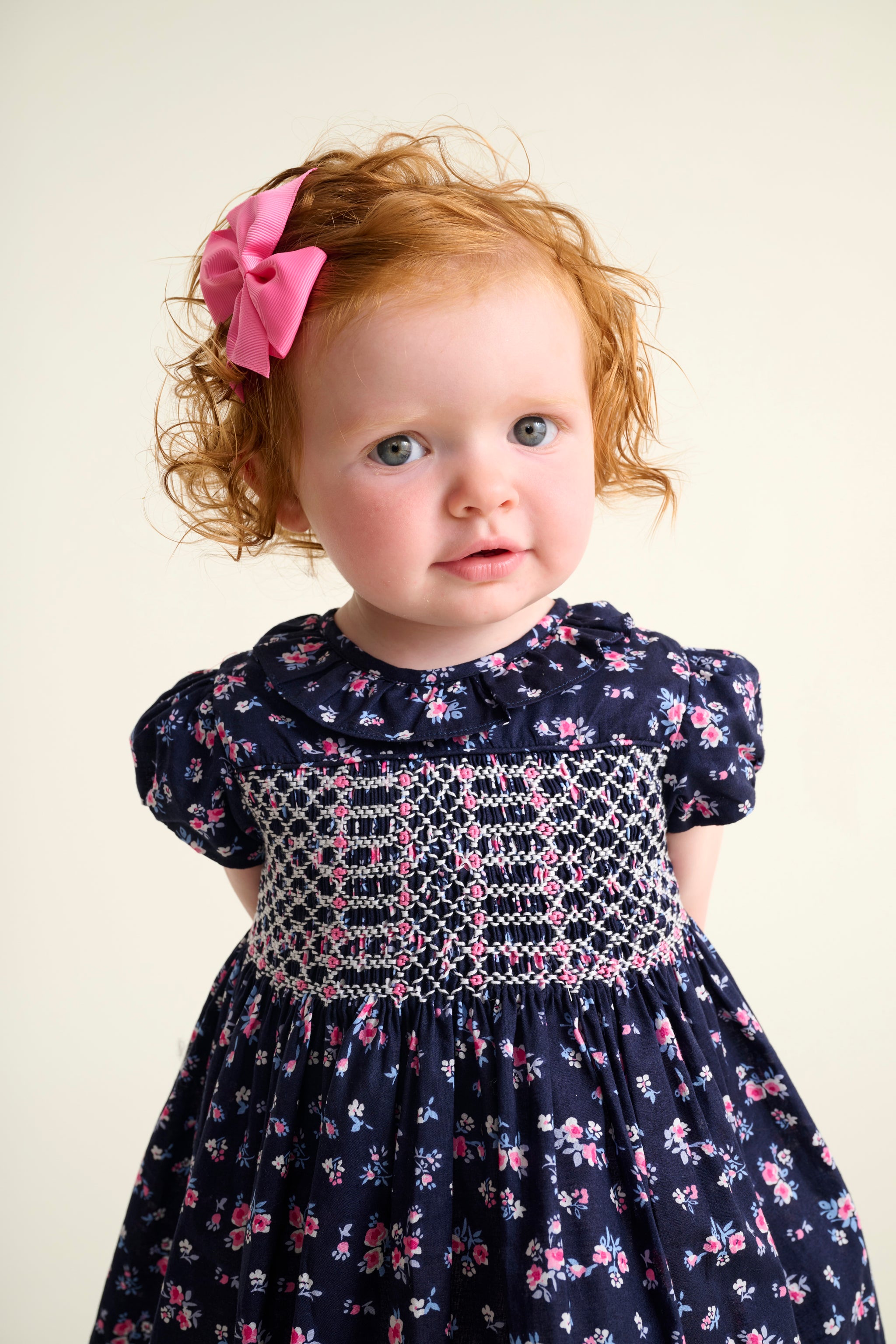 toddler girl wearing a navy blue dress with floral patterns and a pink bow in hair.