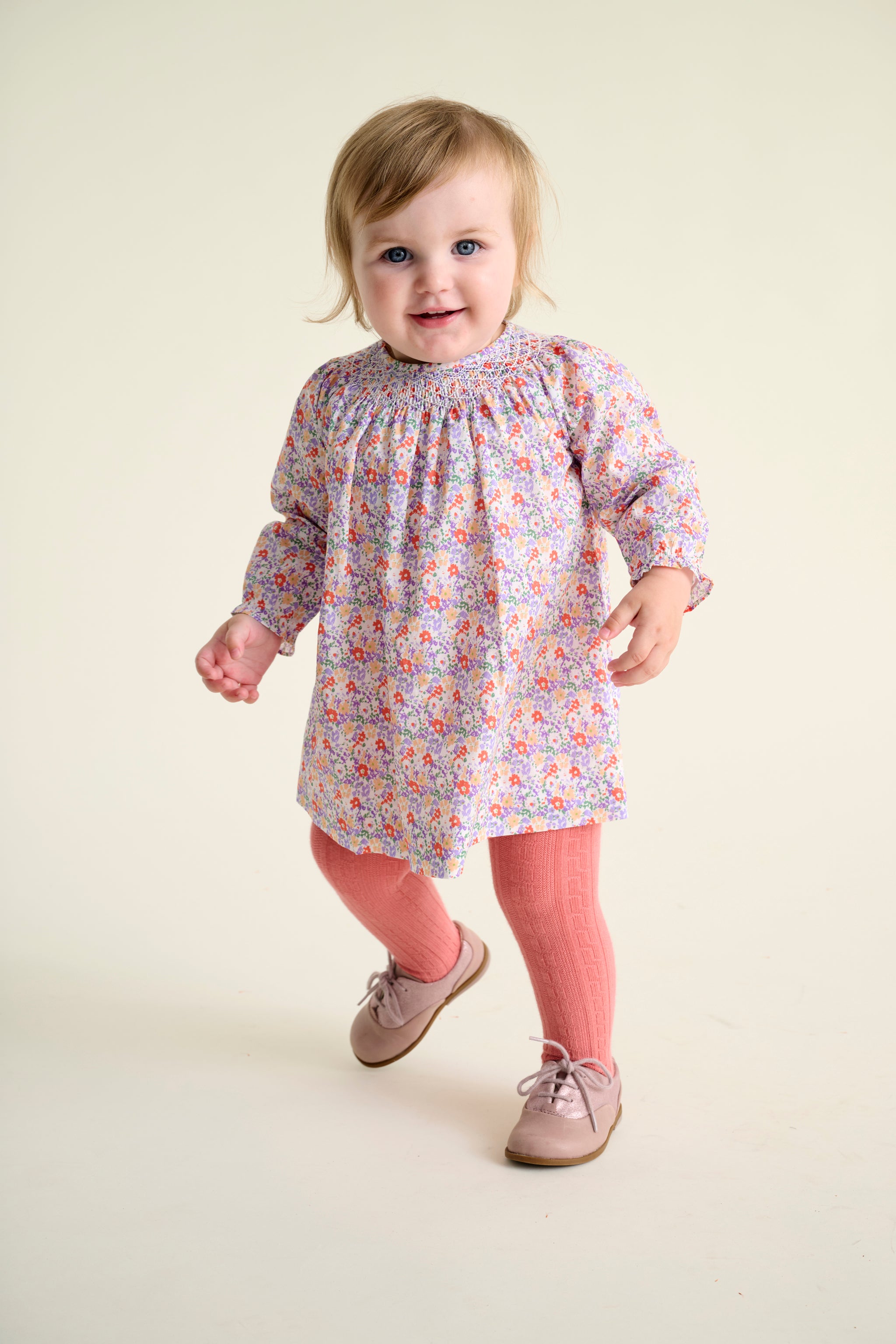 baby wearing a floral dress and pink leggings on a beige background