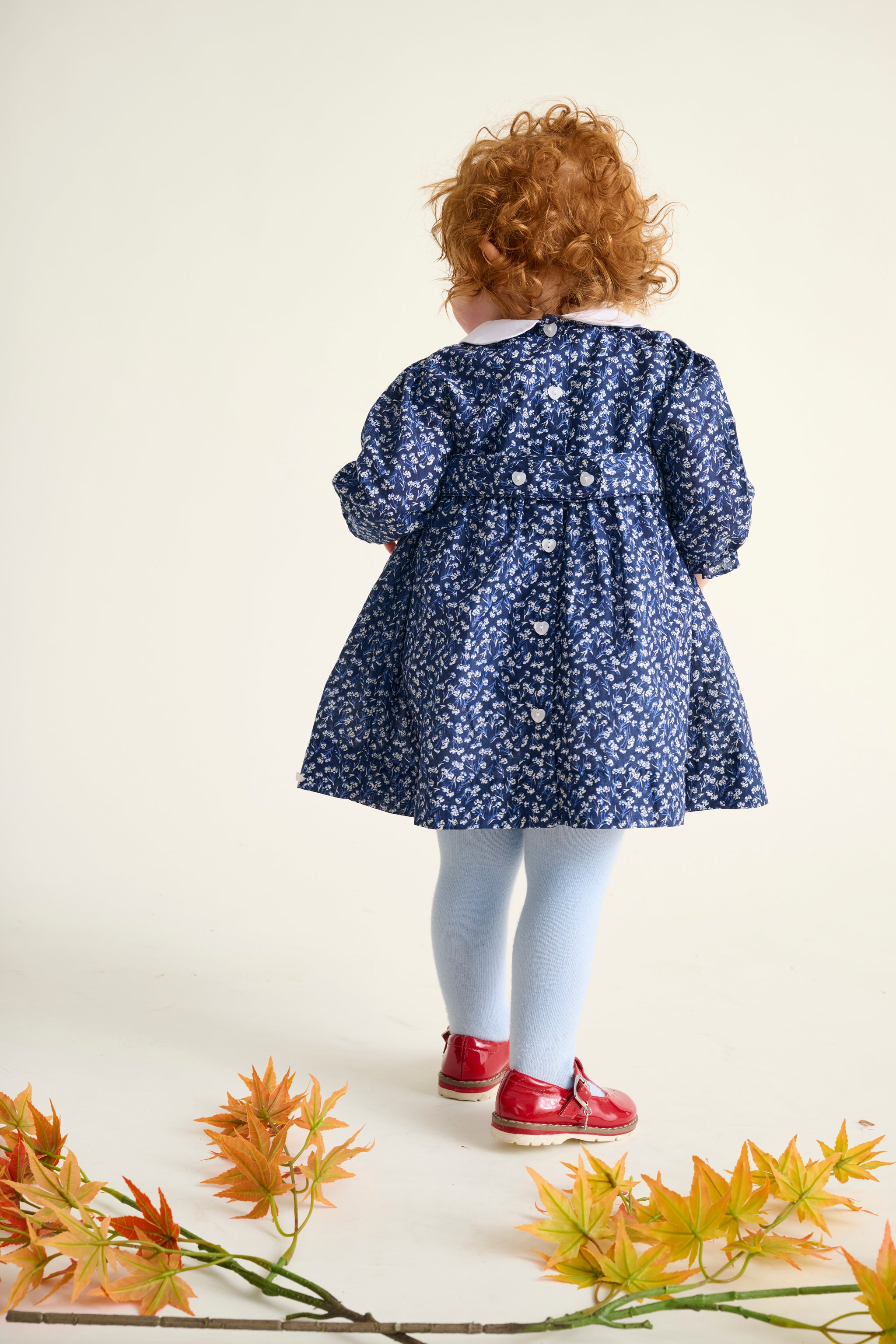 back view of child wearing a blue floral dress with white heart buttons