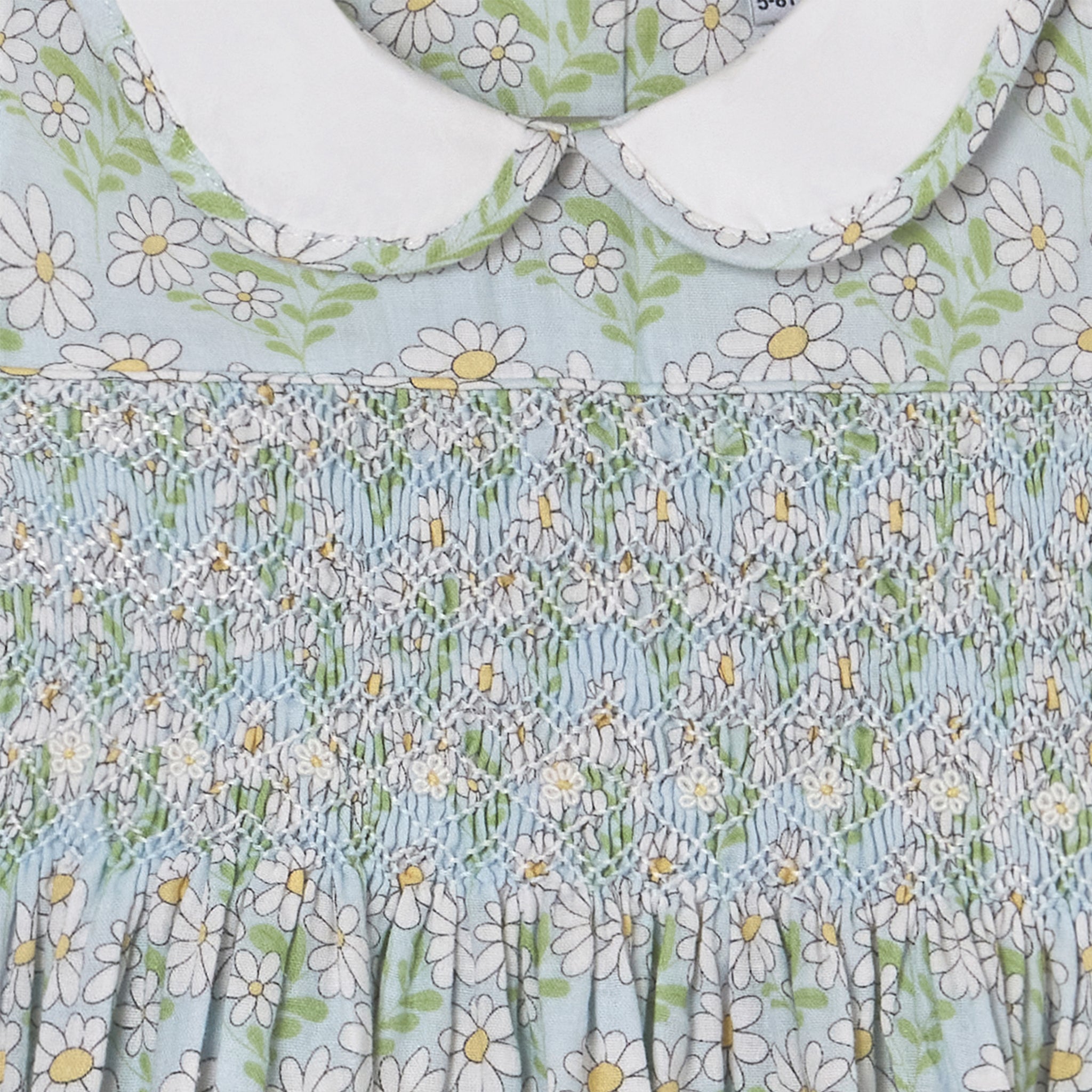 Floral patterned fabric with white flowers and green leaves on a light blue background featuring hand-smocked detail