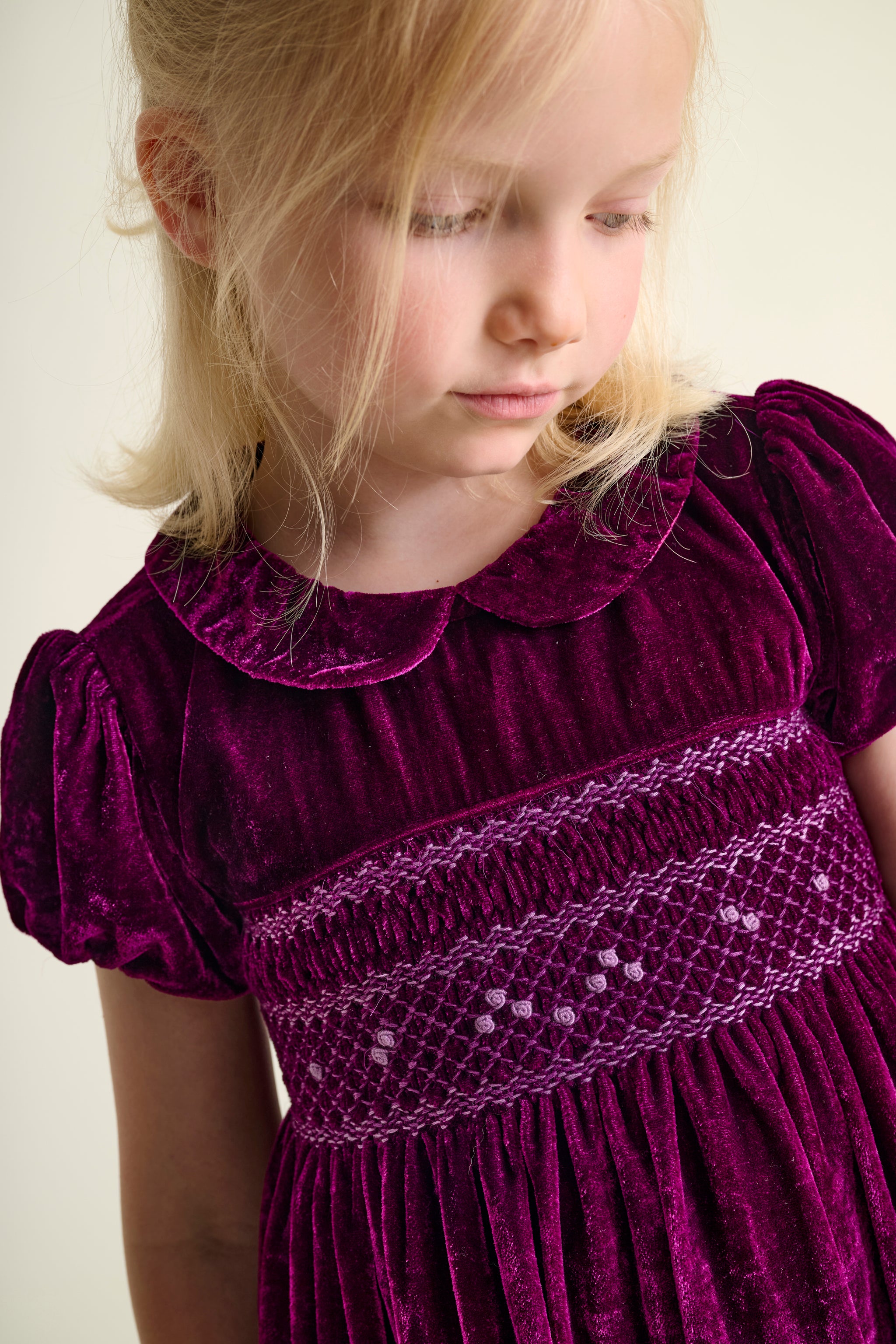 Young girl wearing a burgundy velvet dress with hand-embroidery and smocking close-up