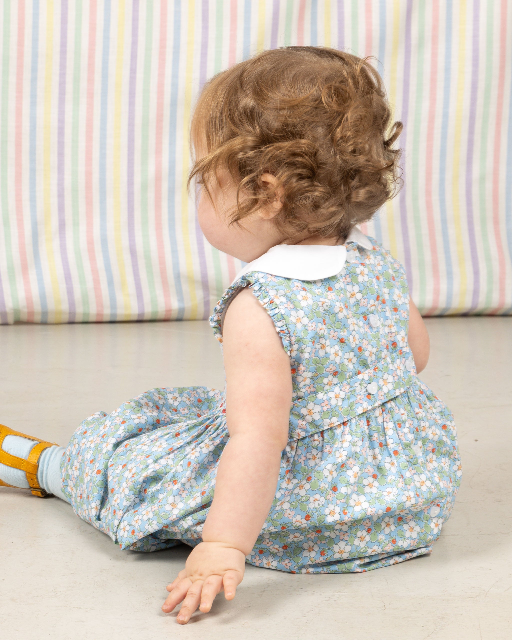 baby sitting, wearing Liberty fabric, hand-smocked baby dress, strawberry print, baby blue