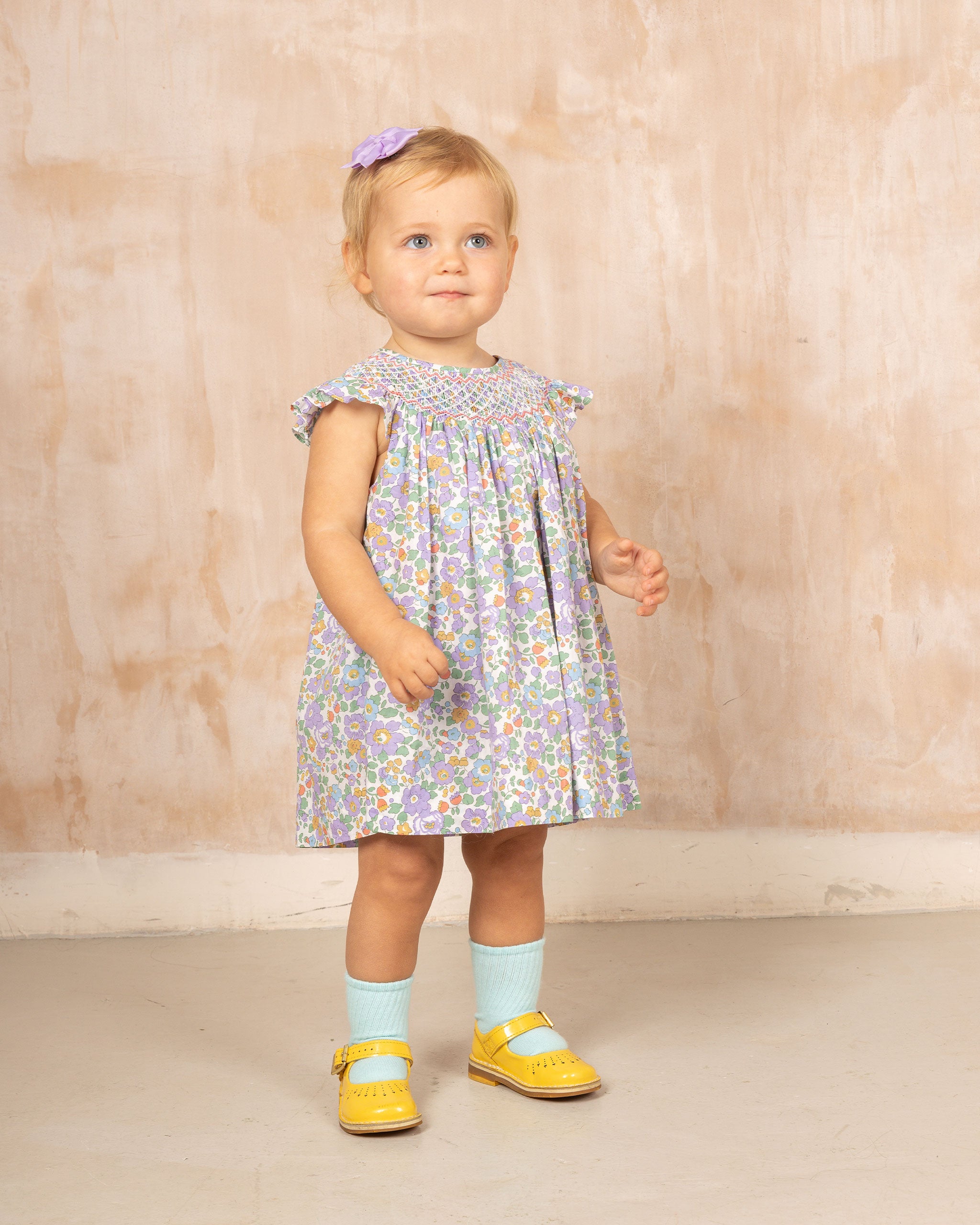 Toddler wearing  a Smocked baby dress made form  Liberty purple Betsy fabric 