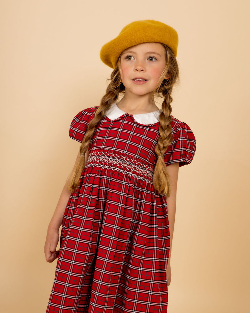child model wearing hand-smocked tartan dress with white collar with piping