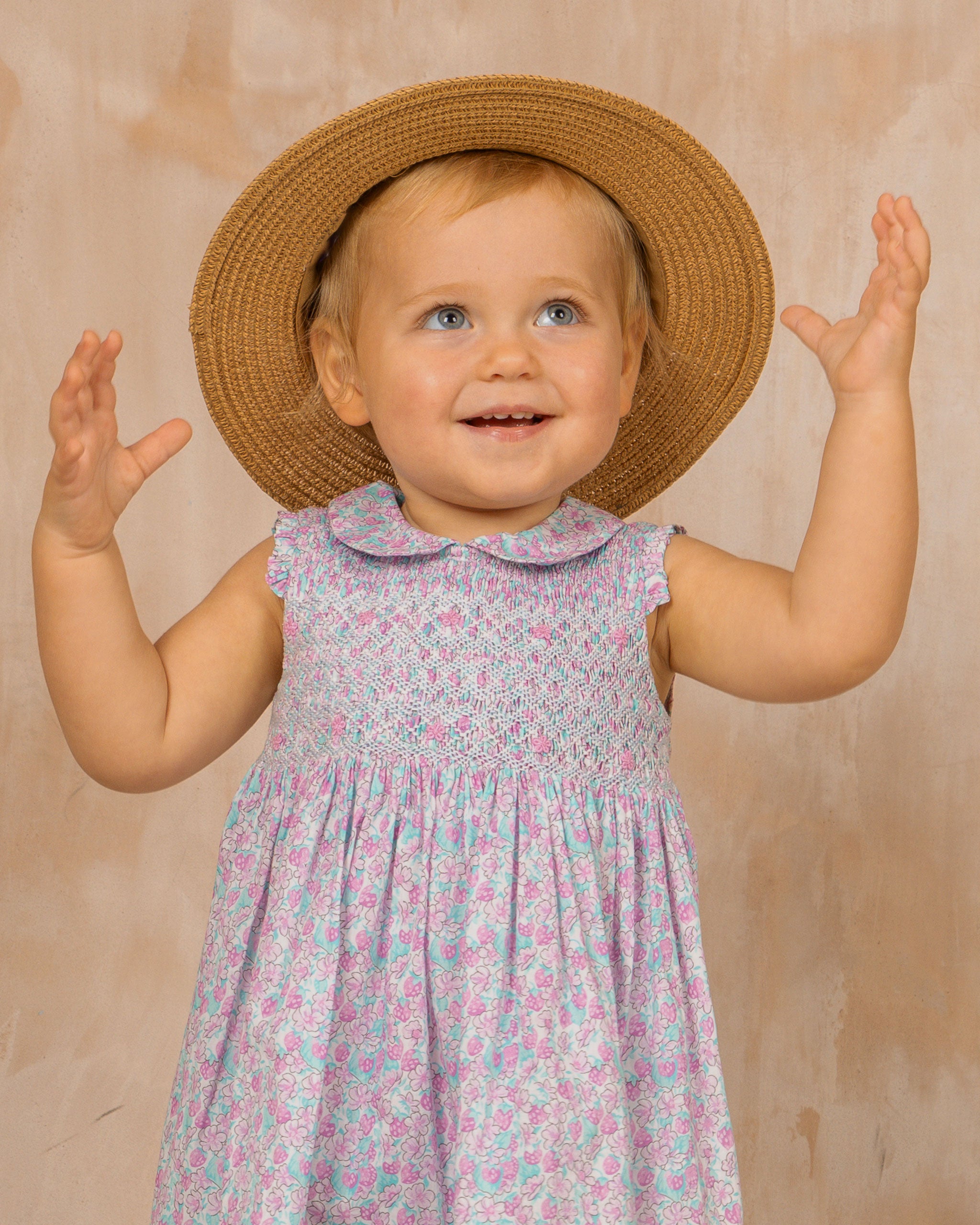 baby in smock dress smiling and wearing a sun hat