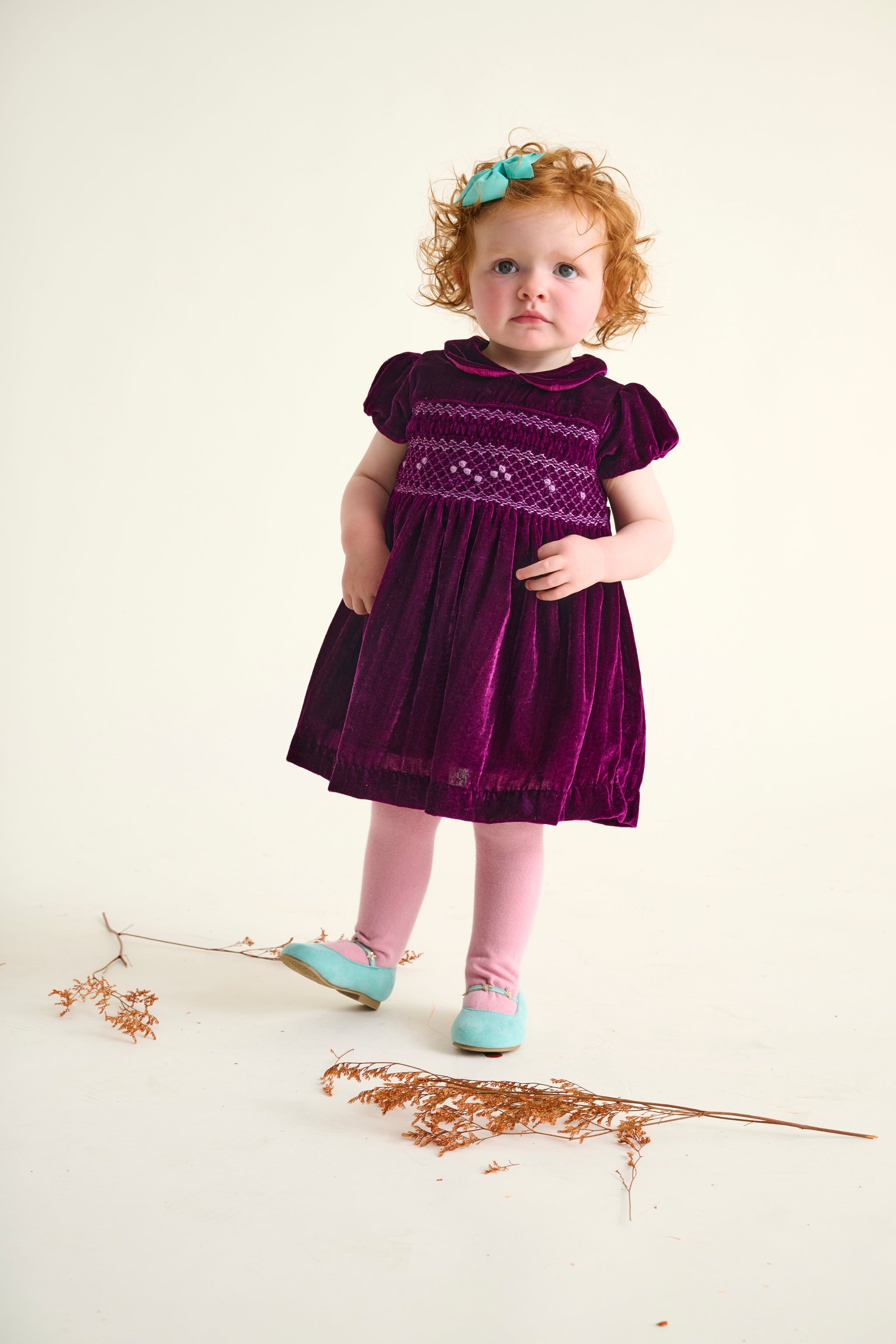 Toddler girl wearing a burgundy velvet dress with hand-smocked bodice