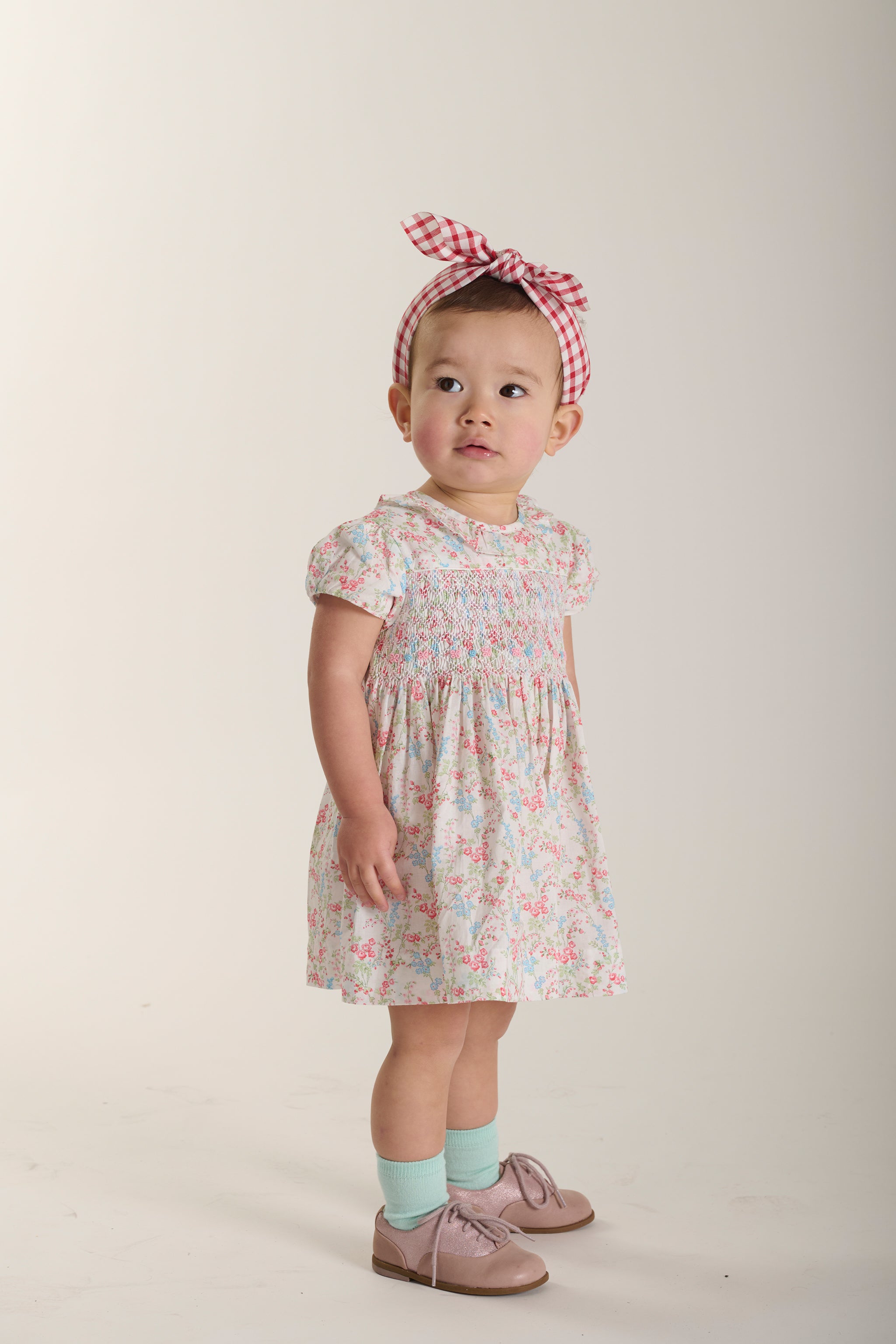 Baby wearing a floral smock dress and headband on a plain background
