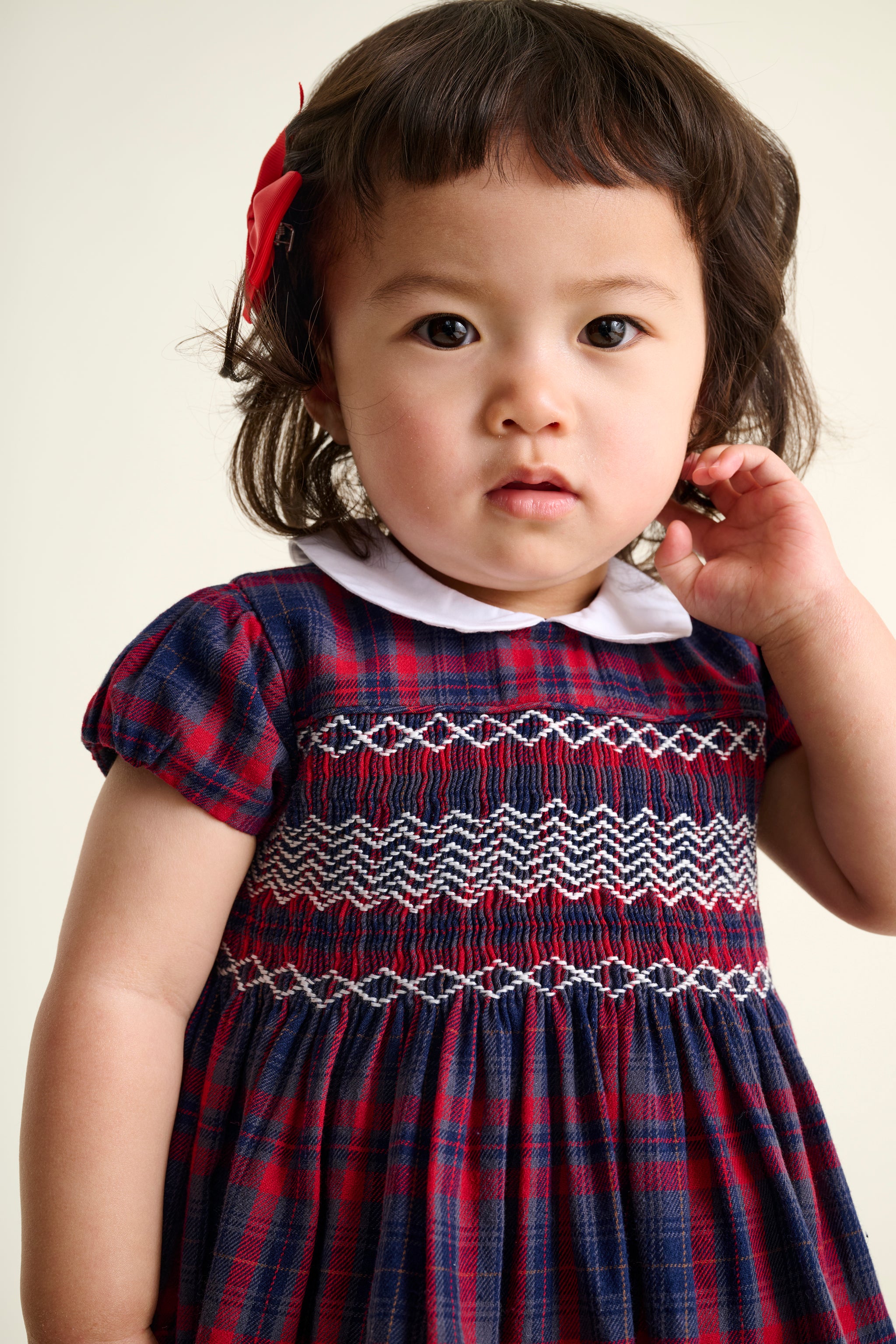 Toddler wearing a hand-smocked red and blue tartan dress with a white collar.