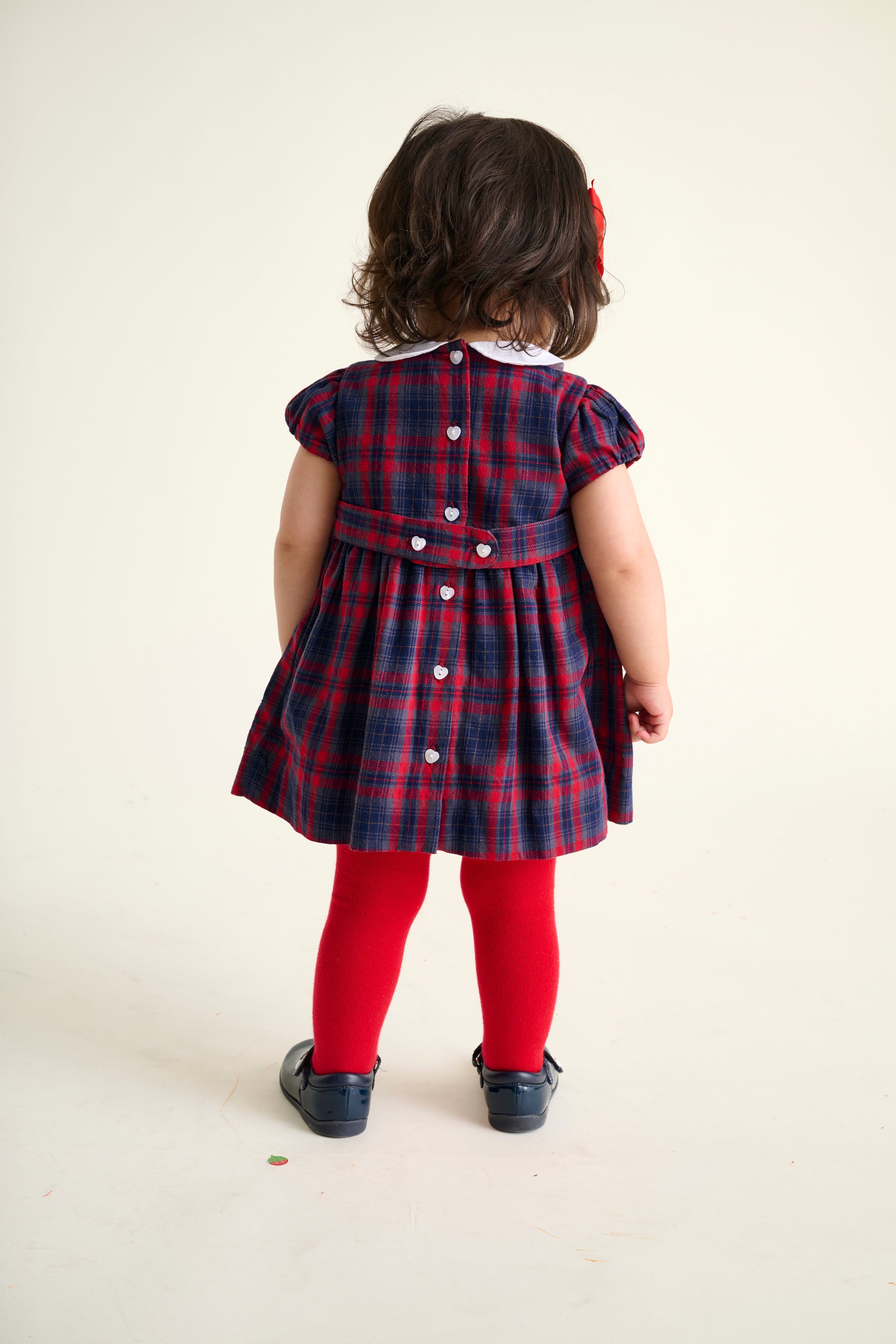 Toddler wearing a red and blue tartan  dress on a white background