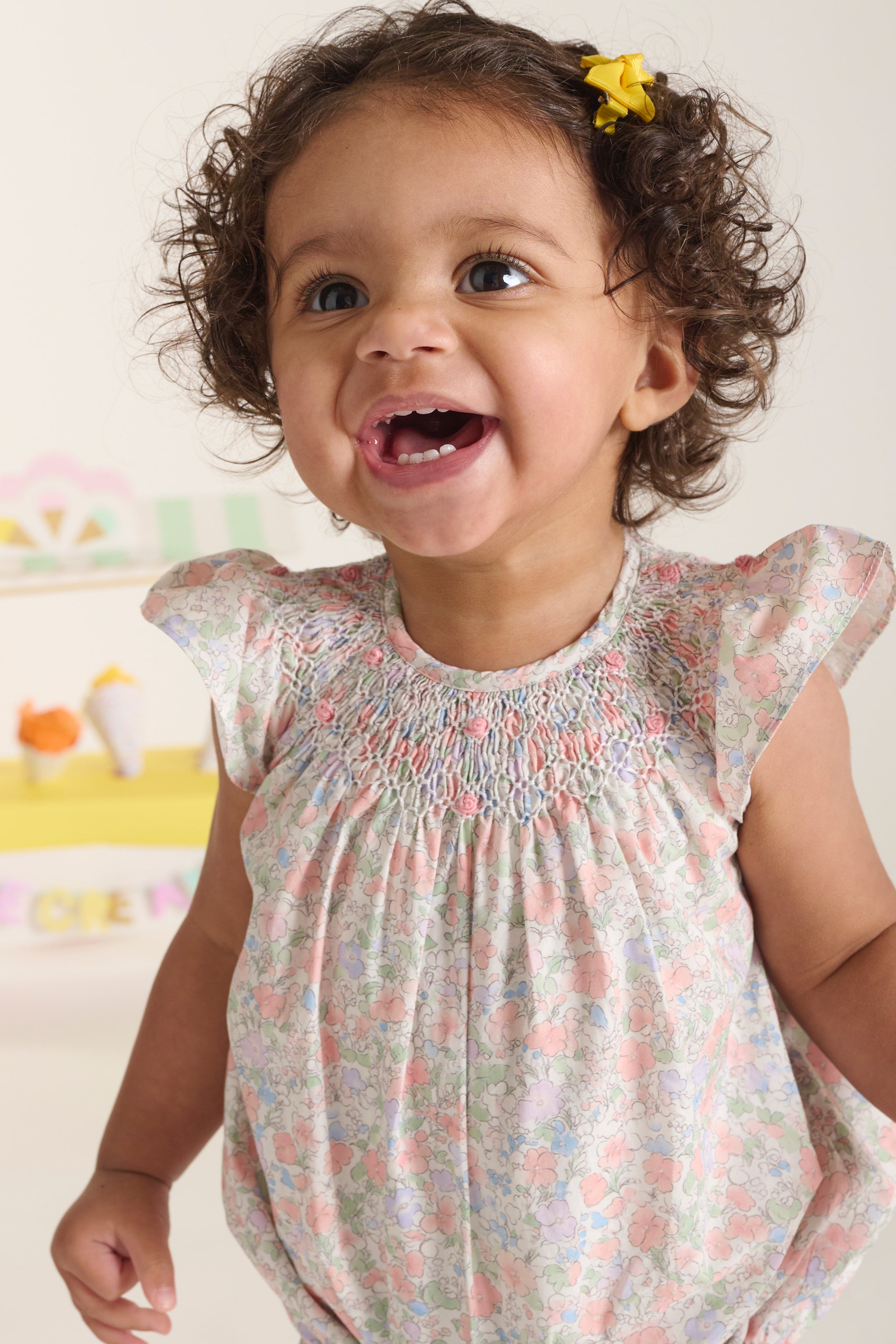 Child wearing a floral baby roper with a hand-smocked neckline