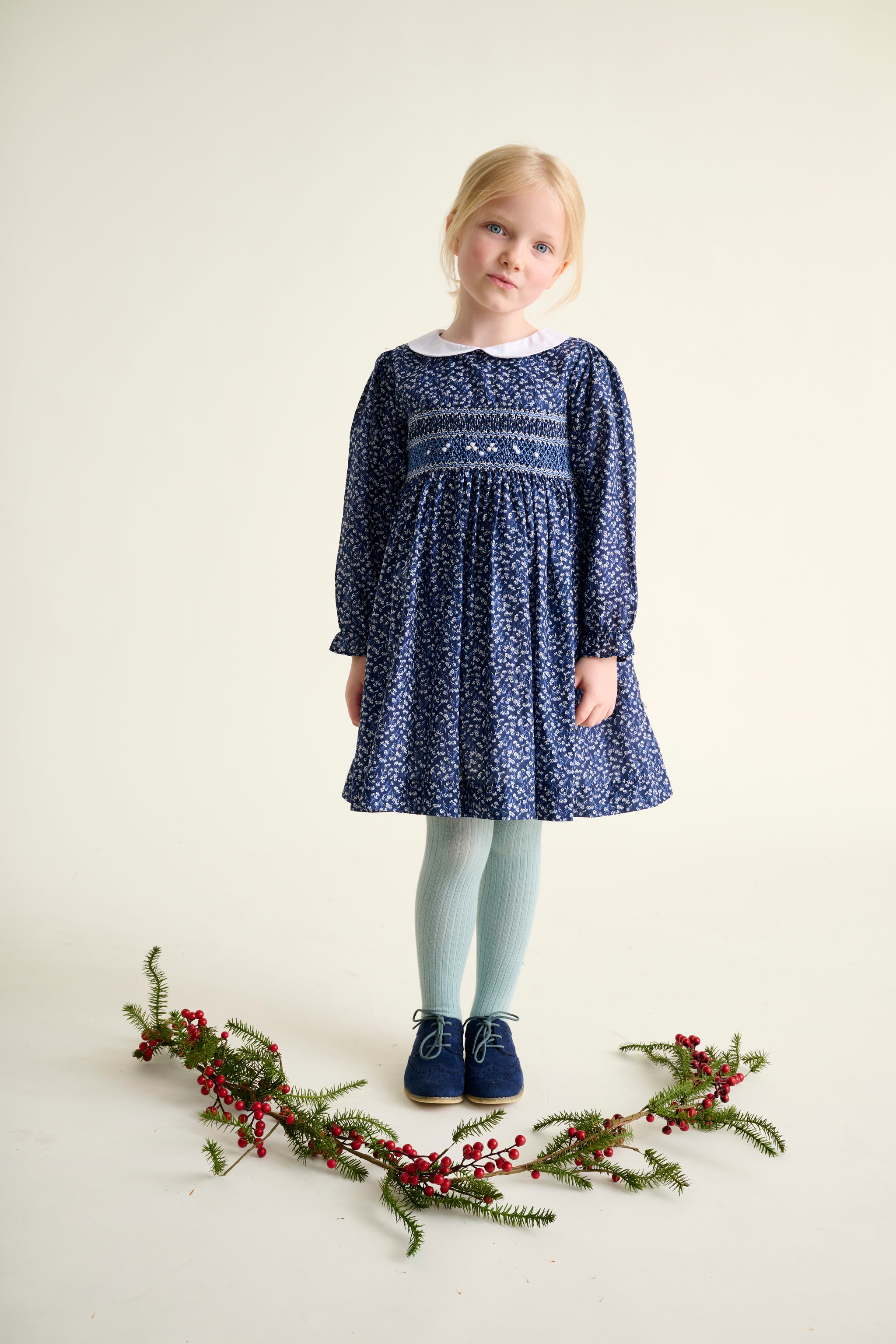 Young girl wearing a long-sleeved blue patterned dress with hand-smocking and white Peter Pan collar