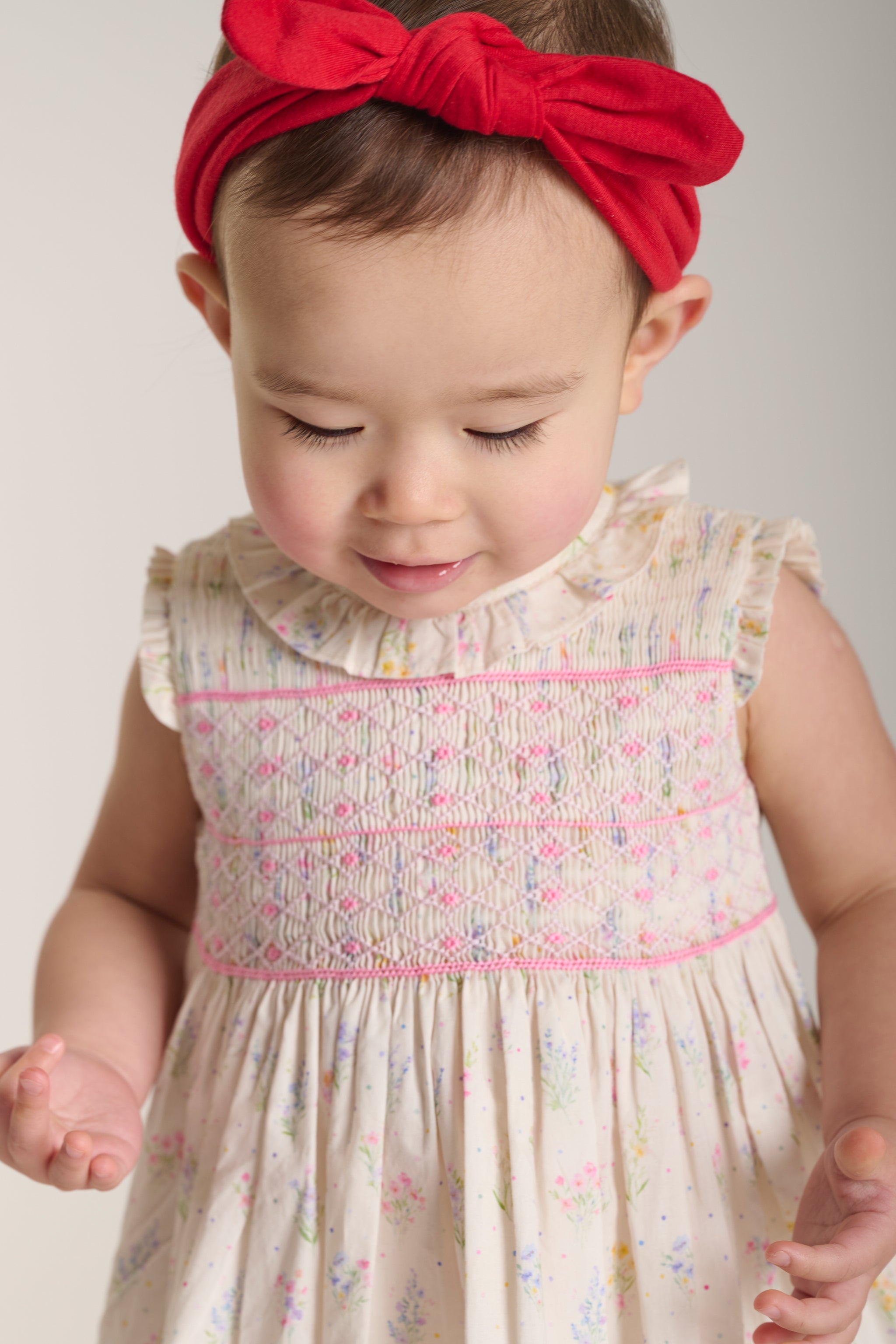 Baby wearing a floral smock dress with a red headband 