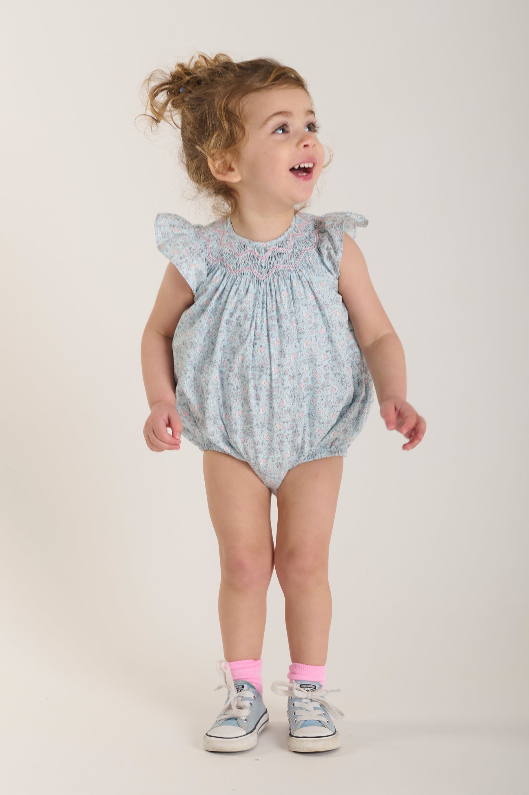 Child wearing a light blue romper with ruffled sleeves and bird design
