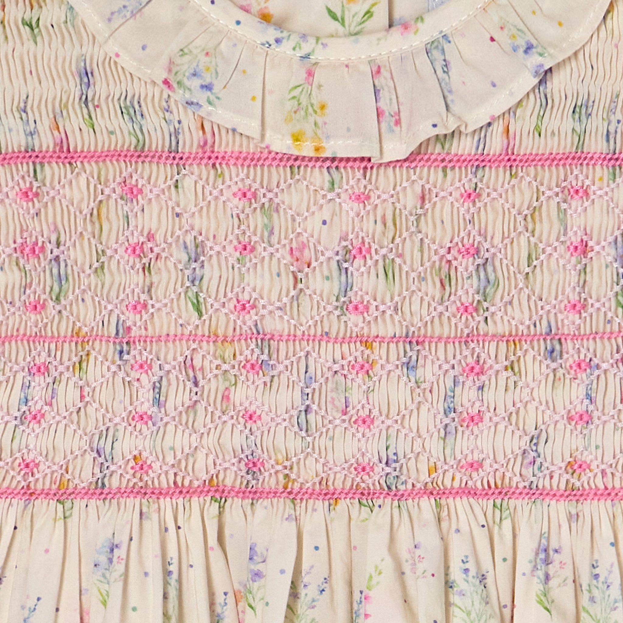 Close-up of a fabric with flower patterns and pink smocking  on a beige background