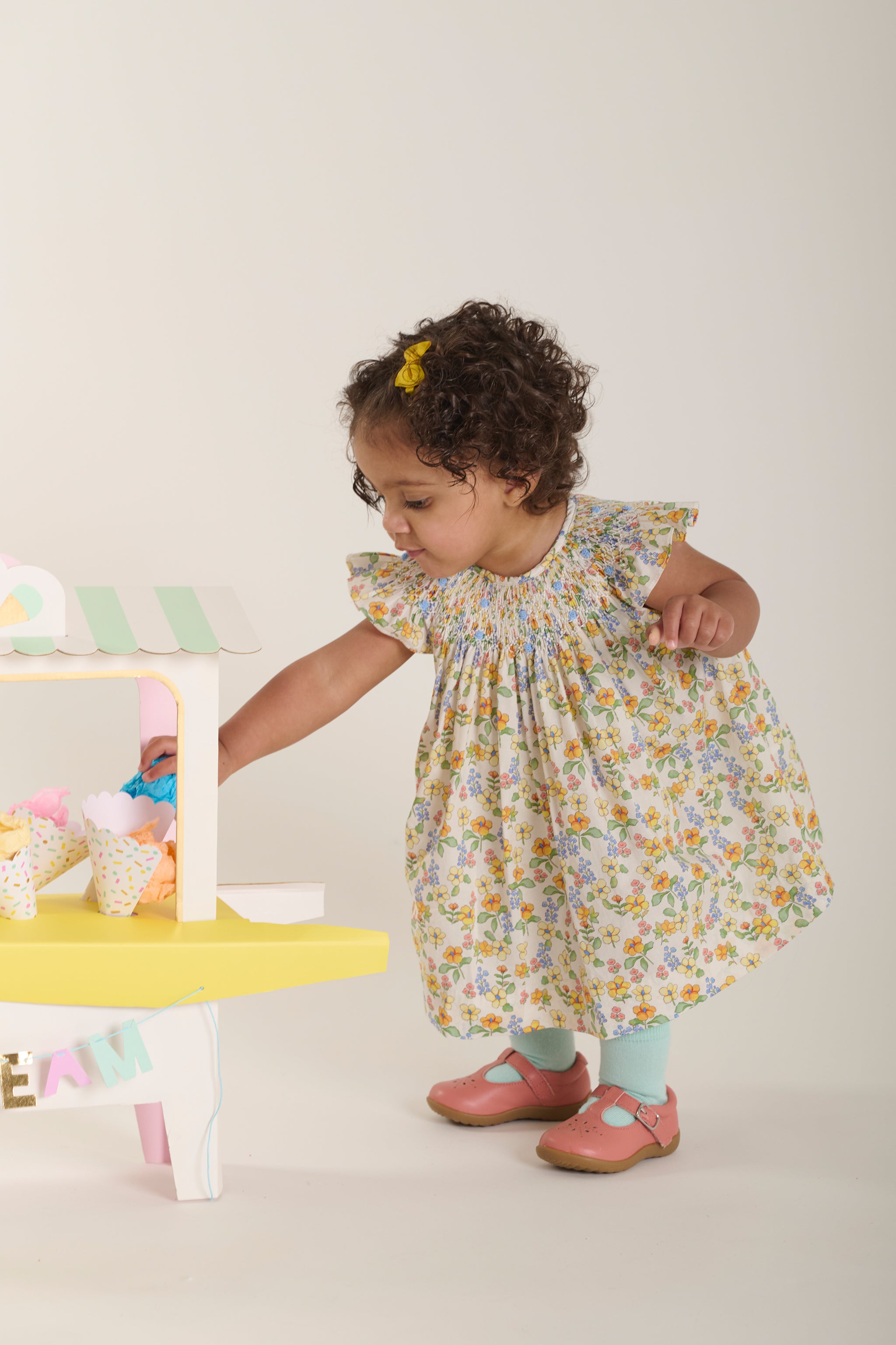Child in a floral dress playing with a toy kitchen set on a white background