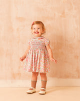smiling baby girl in Liberty print dress with hand smocking